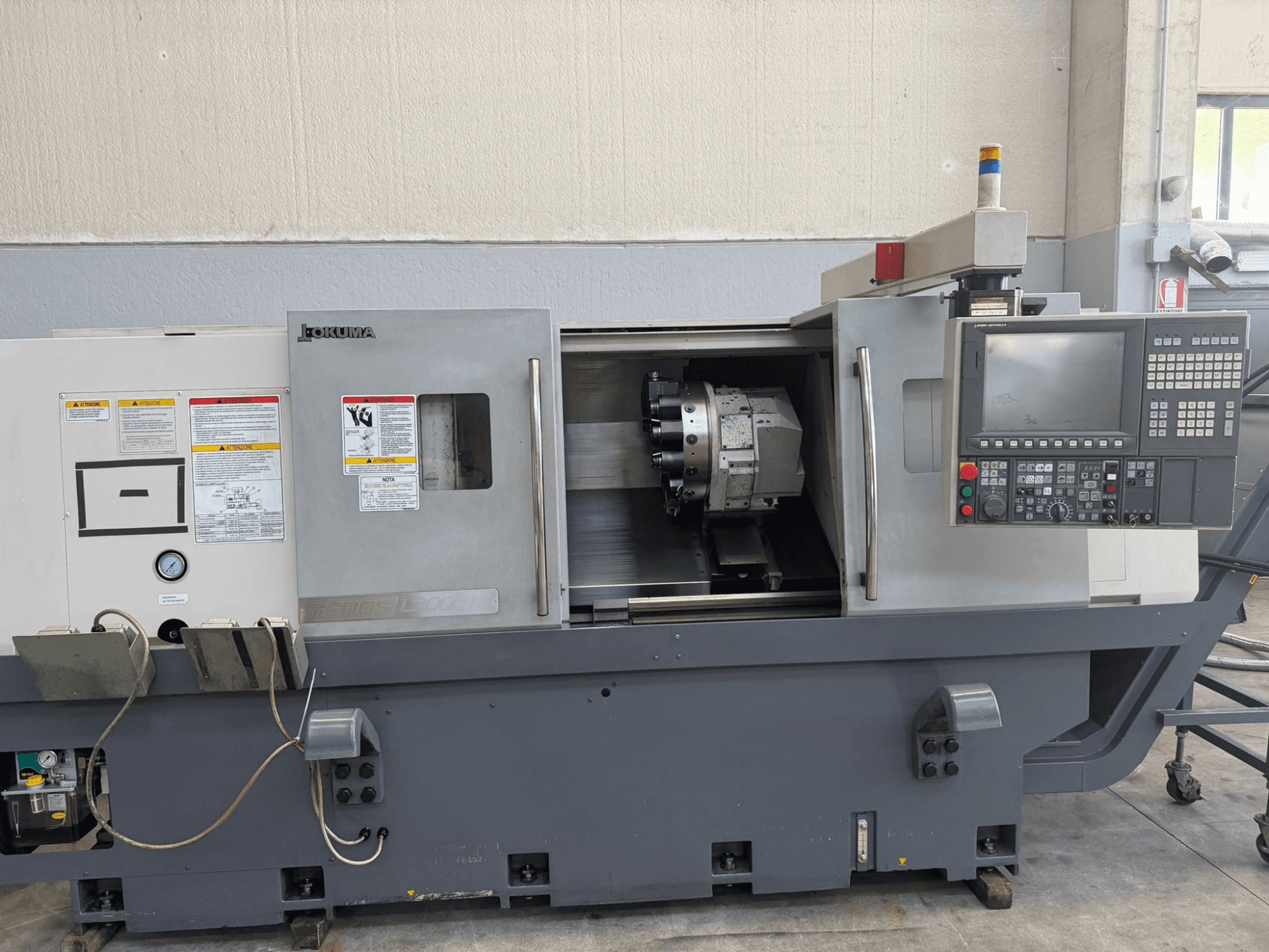 Токарный станок с ЧПУ Okuma, вид спереди, на панели управления, держатель режущего инструмента и предупреждения о безопасности сбоку.