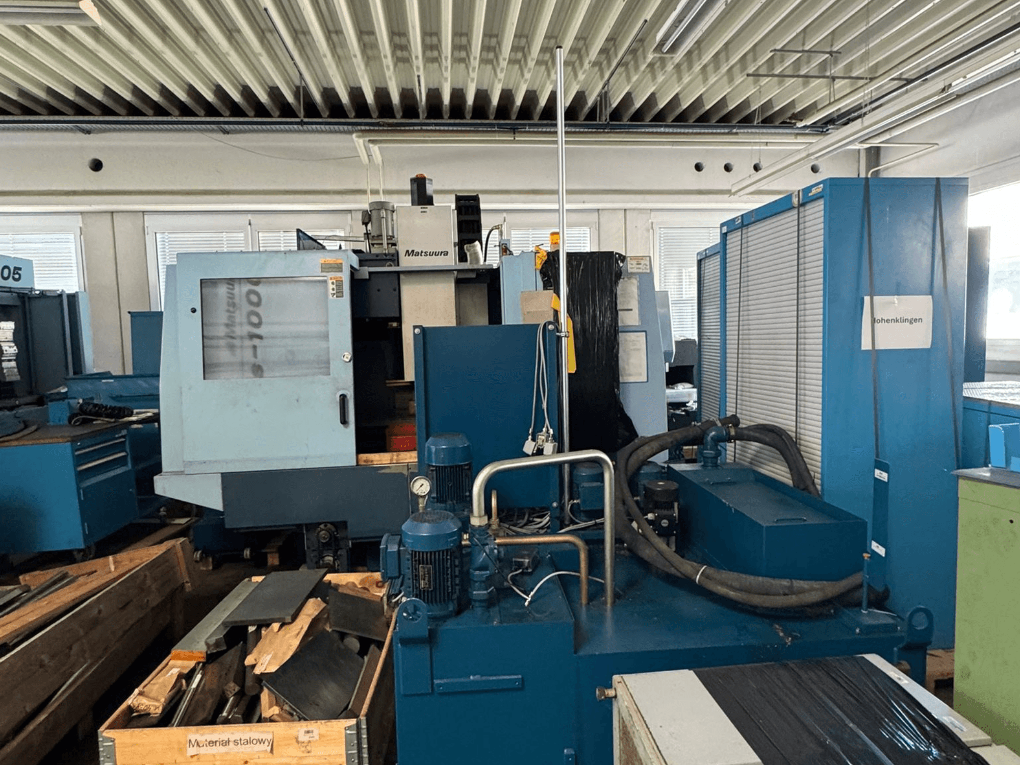 Вид спереди на вертикальный обрабатывающий центр Matsuura Vplus 1000/40 с изображением элементов управления, двигателей и окружающей производственной обстановки.