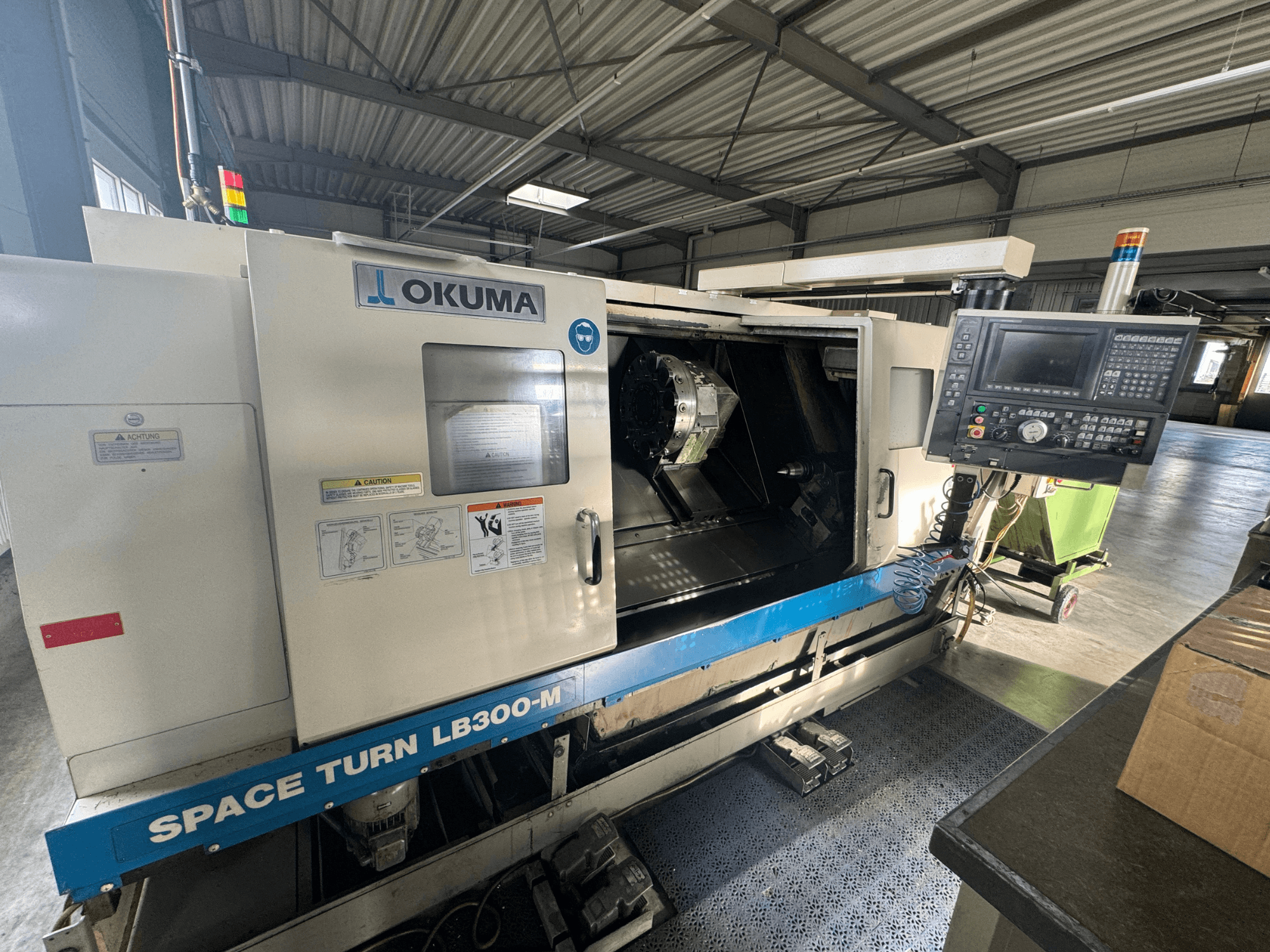 Токарный станок с ЧПУ Okuma Space Turn LB300-M с видом спереди, с панелью управления и открытой дверью, открывающей внутреннюю зону обработки.