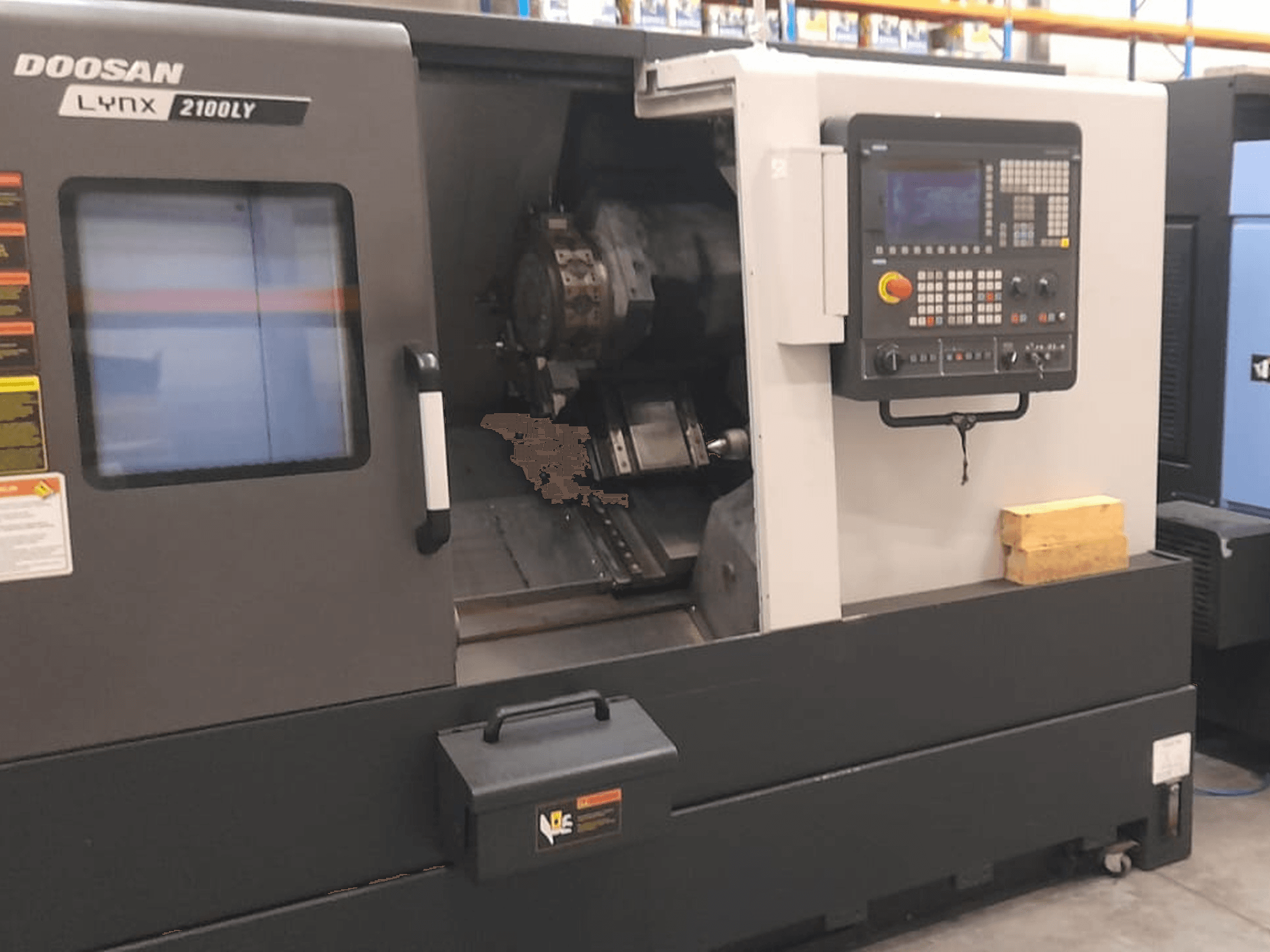 Токарный станок с ЧПУ Doosan Lynx 2100LY, вид спереди, демонстрирующий панель управления, держатель инструмента и внутреннее рабочее пространство; видны технические наклейки.