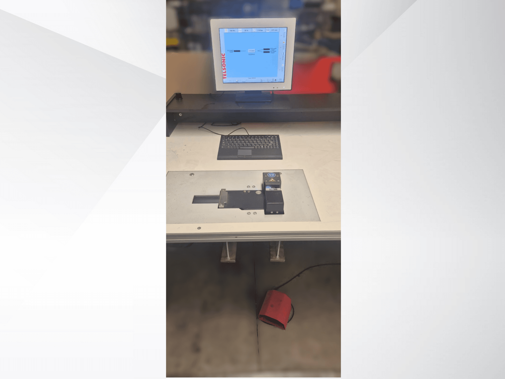 Вид сверху вниз на испытательную станцию с компьютерным монитором, клавиатурой и панелью управления с кнопкой и зеленым индикатором.