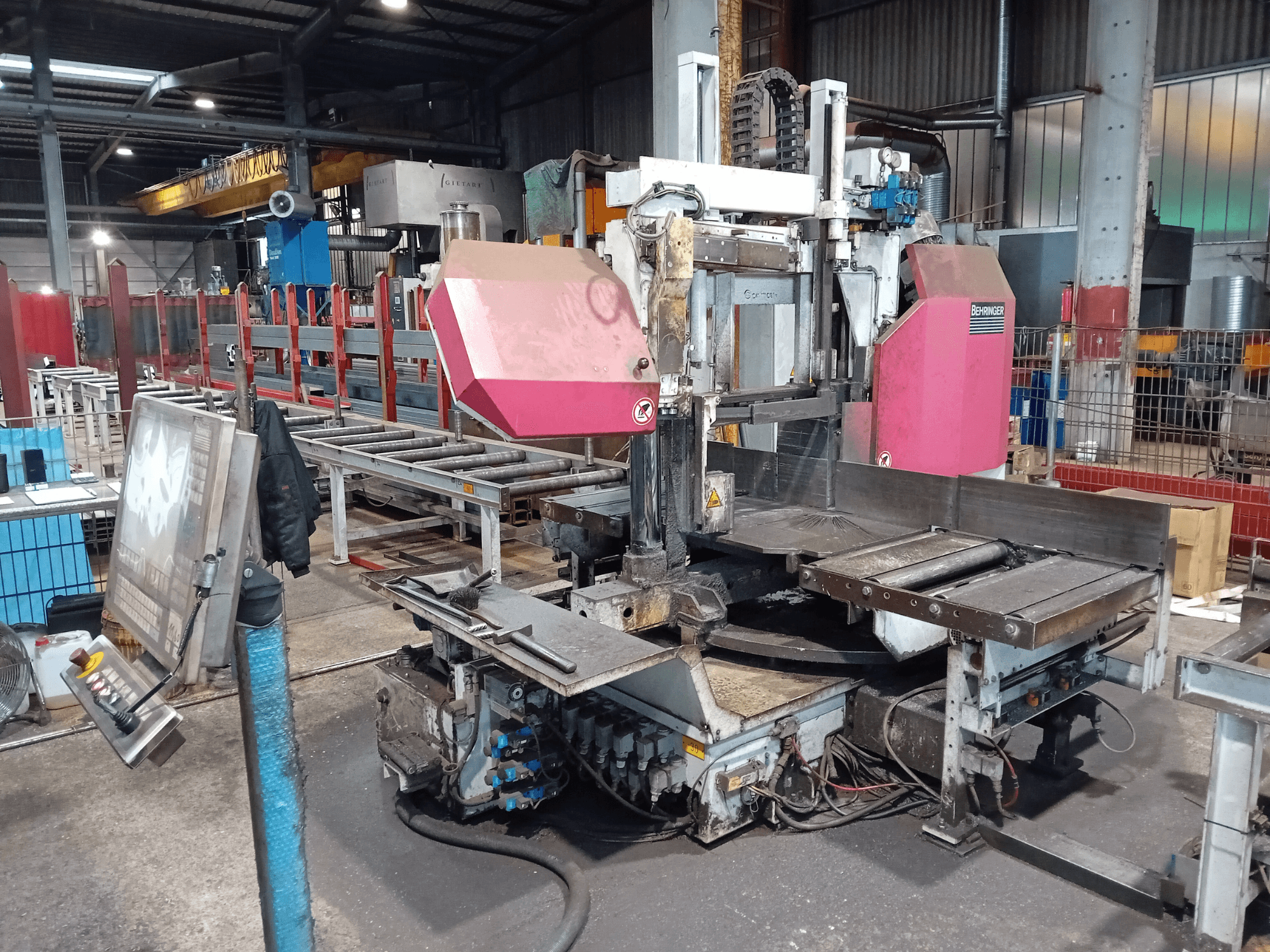 Ленточнопильный станок Behringer на заводе, вид спереди, с большим режущим полотном и панелью управления с кнопками.