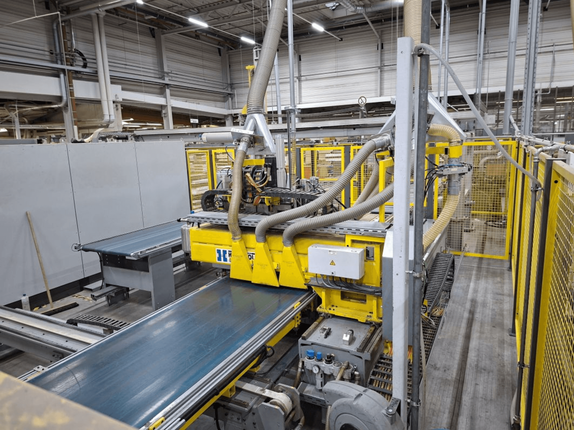 Промышленный конвейер с видом сбоку, на котором изображены желтые механизмы, панель управления и насадки для шлангов для производства.
