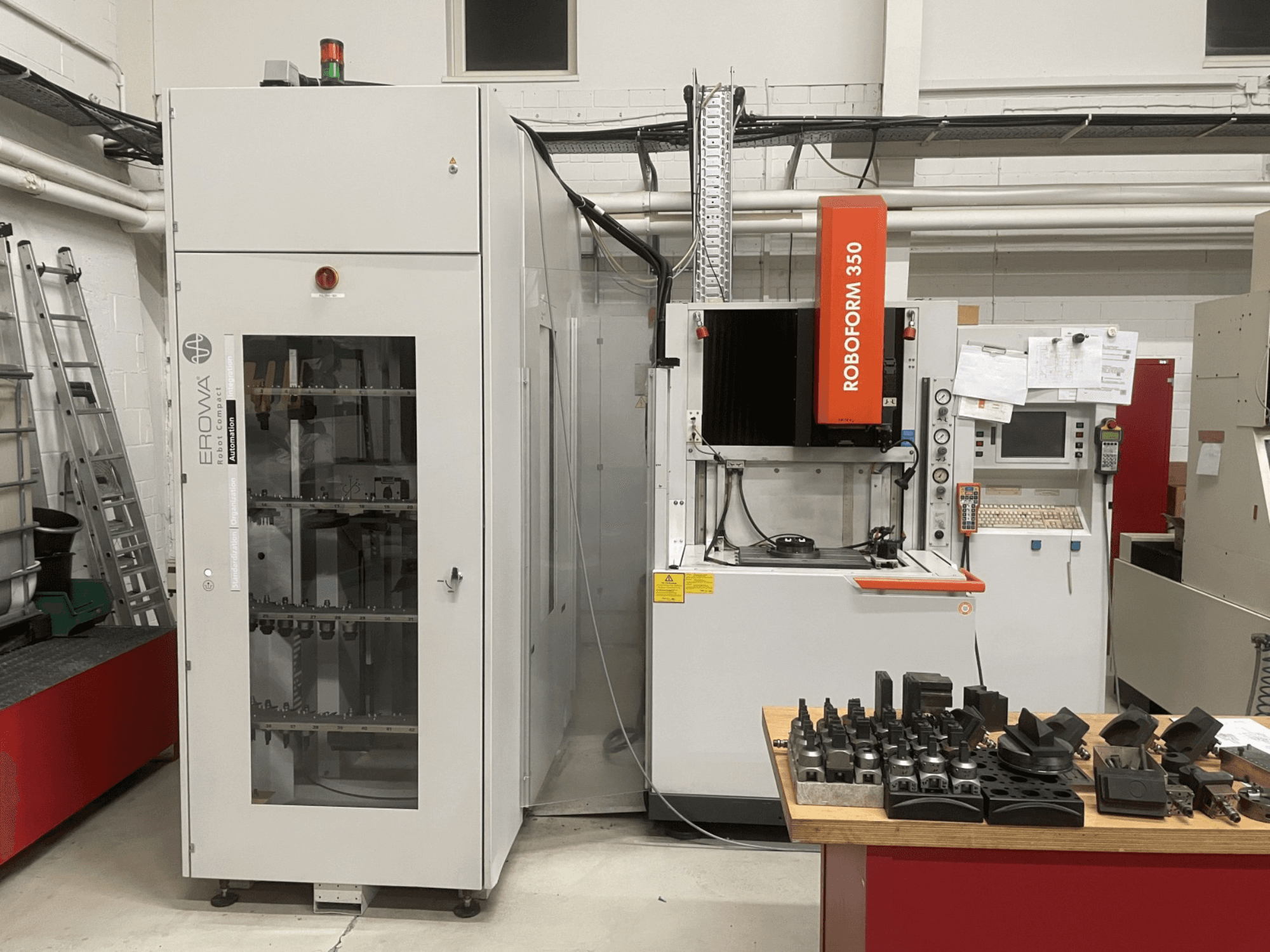 Станок CHARMILLES Roboform 350, вид спереди, с инструментами, выставленными на столе, и соседним оборудованием.