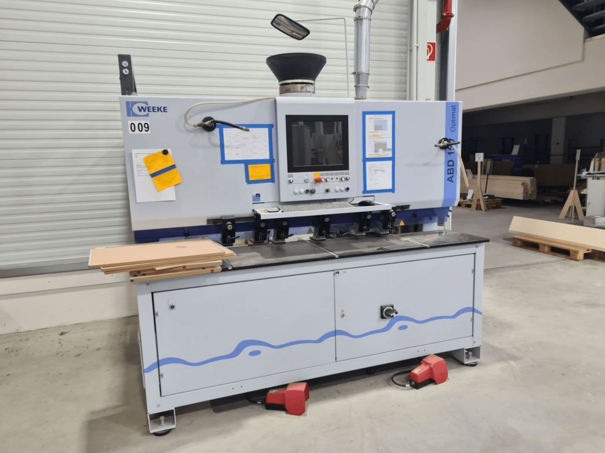 Многошпиндельный сверлильный станок HOMAG WEEKE OPTIMAT ABD150, вид спереди, видны элементы управления и сложенные в стопку деревянные панели.