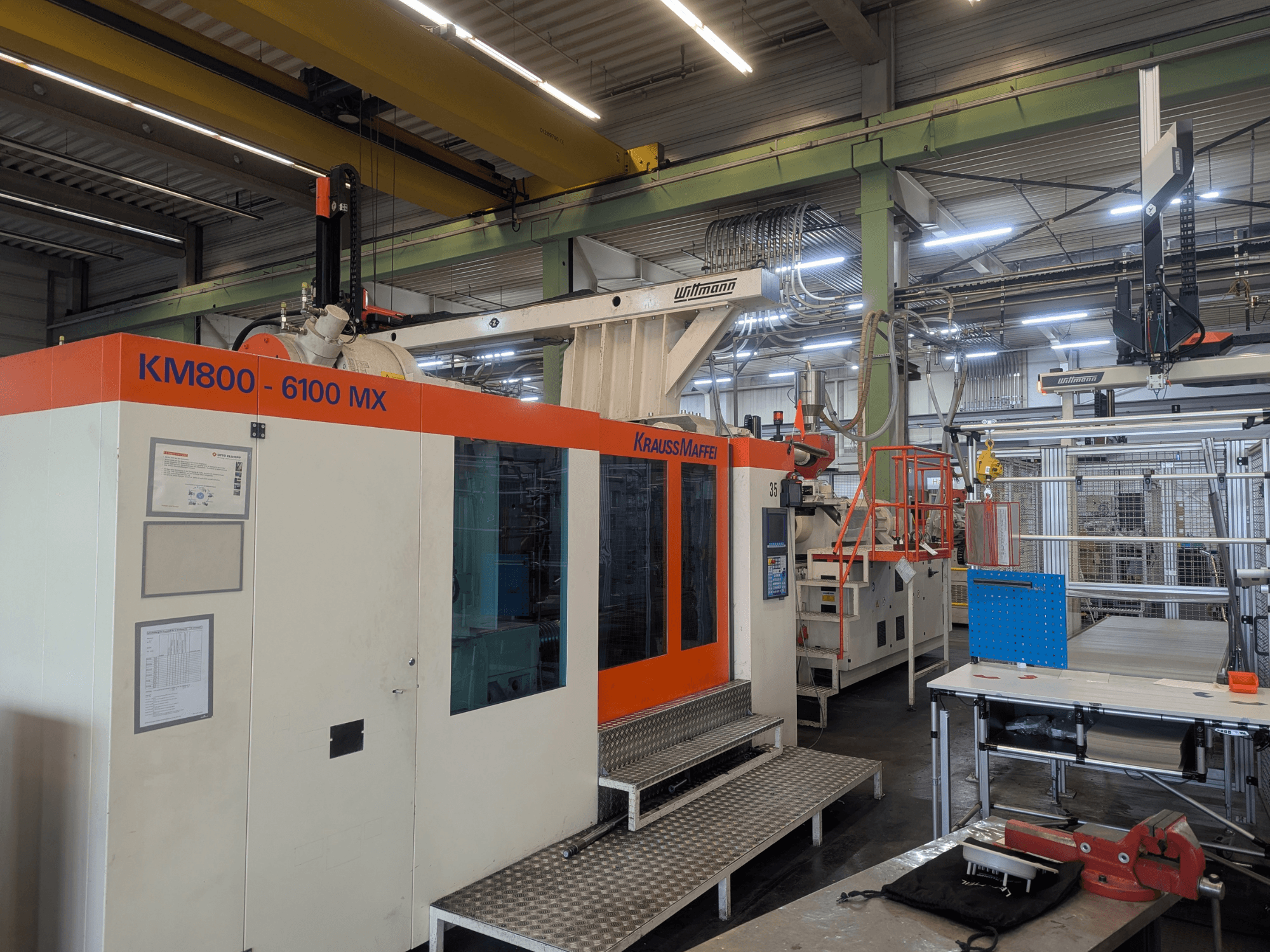 Гидравлический термопластавтомат Krauss Maffei KM 800-6100MX, вид спереди, демонстрирует панель управления и промышленную установку.