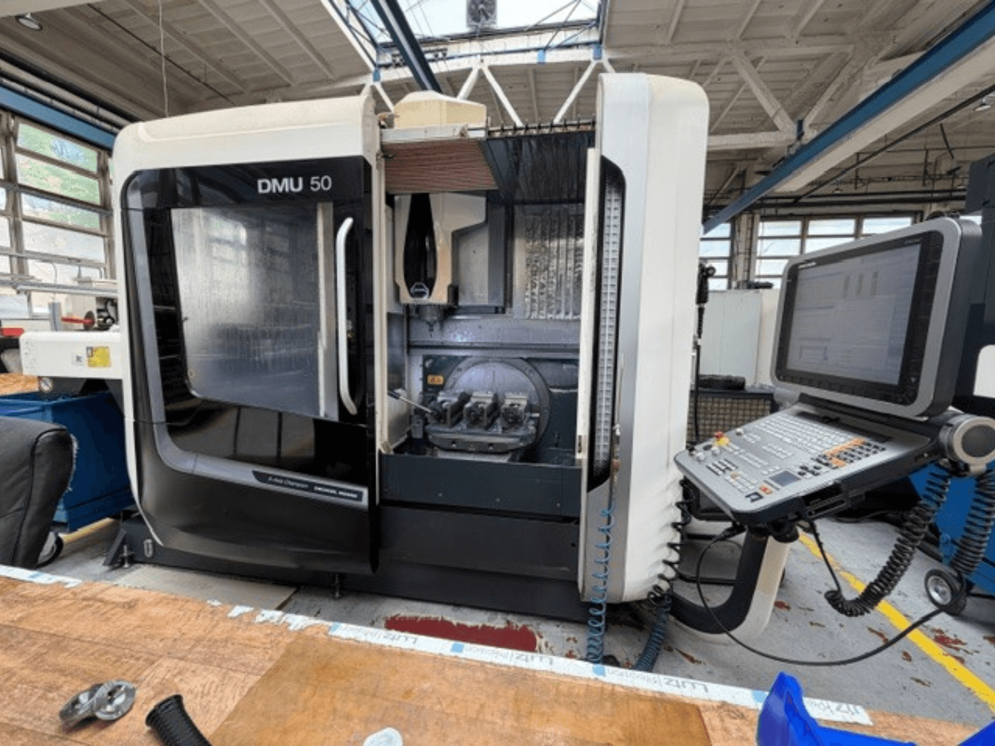 Вертикальный обрабатывающий центр DMG MORI DMU 50 3-го поколения, вид спереди: открытая дверца, видна панель ЧПУ, внутри видна рабочая зона.