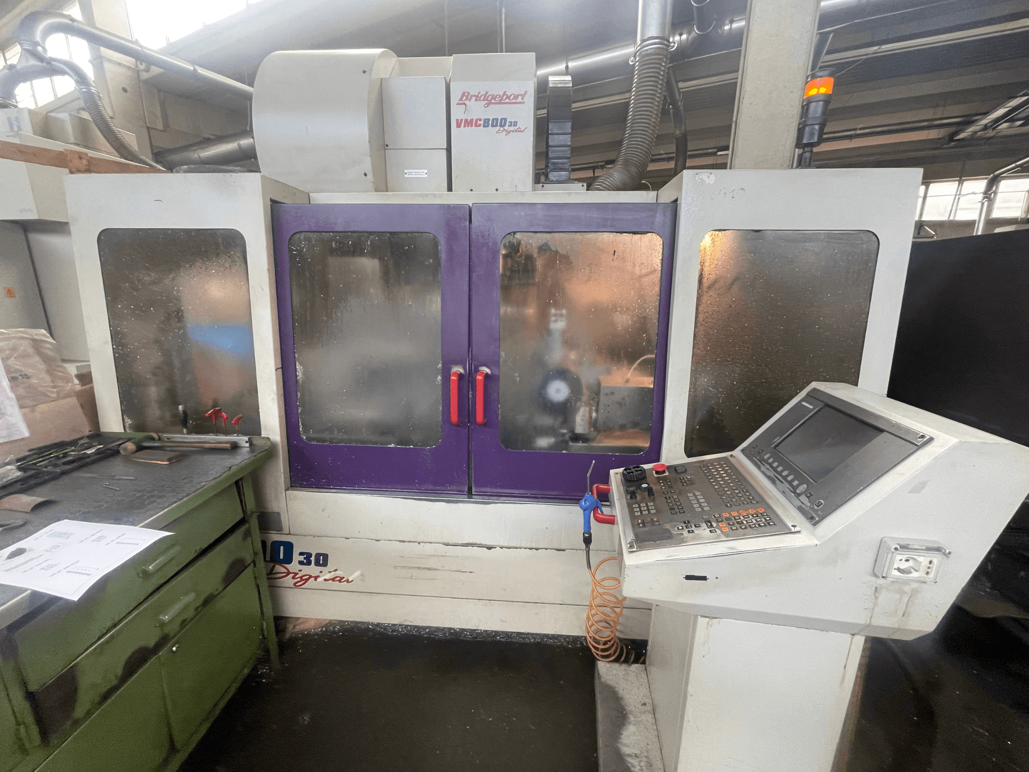 Вертикальный обрабатывающий центр Bridgeport VMC 800/30, вид спереди, на котором видны панель управления и фиолетовые дверцы, а также инструменты на прилегающей поверхности.