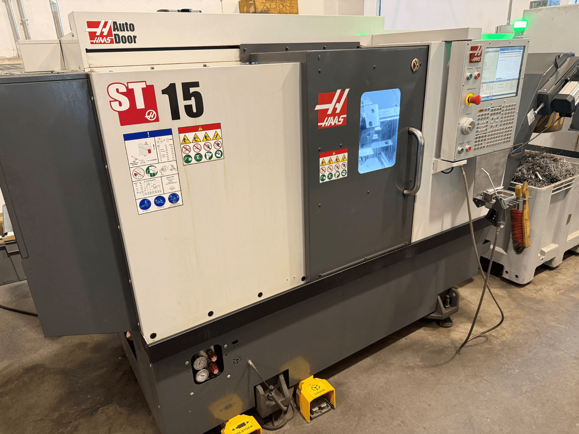 Горизонтальный токарный станок HAAS ST 15, вид спереди с панелью управления, автоматической дверцей и видимыми техническими индикаторами.