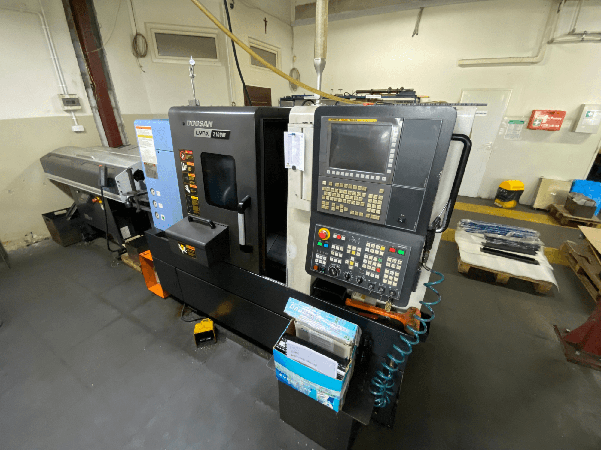 Горизонтальный токарный станок DOOSAN LYNX 2100MA, вид сбоку: на снимке видны панель управления, инструменты и рабочая зона.