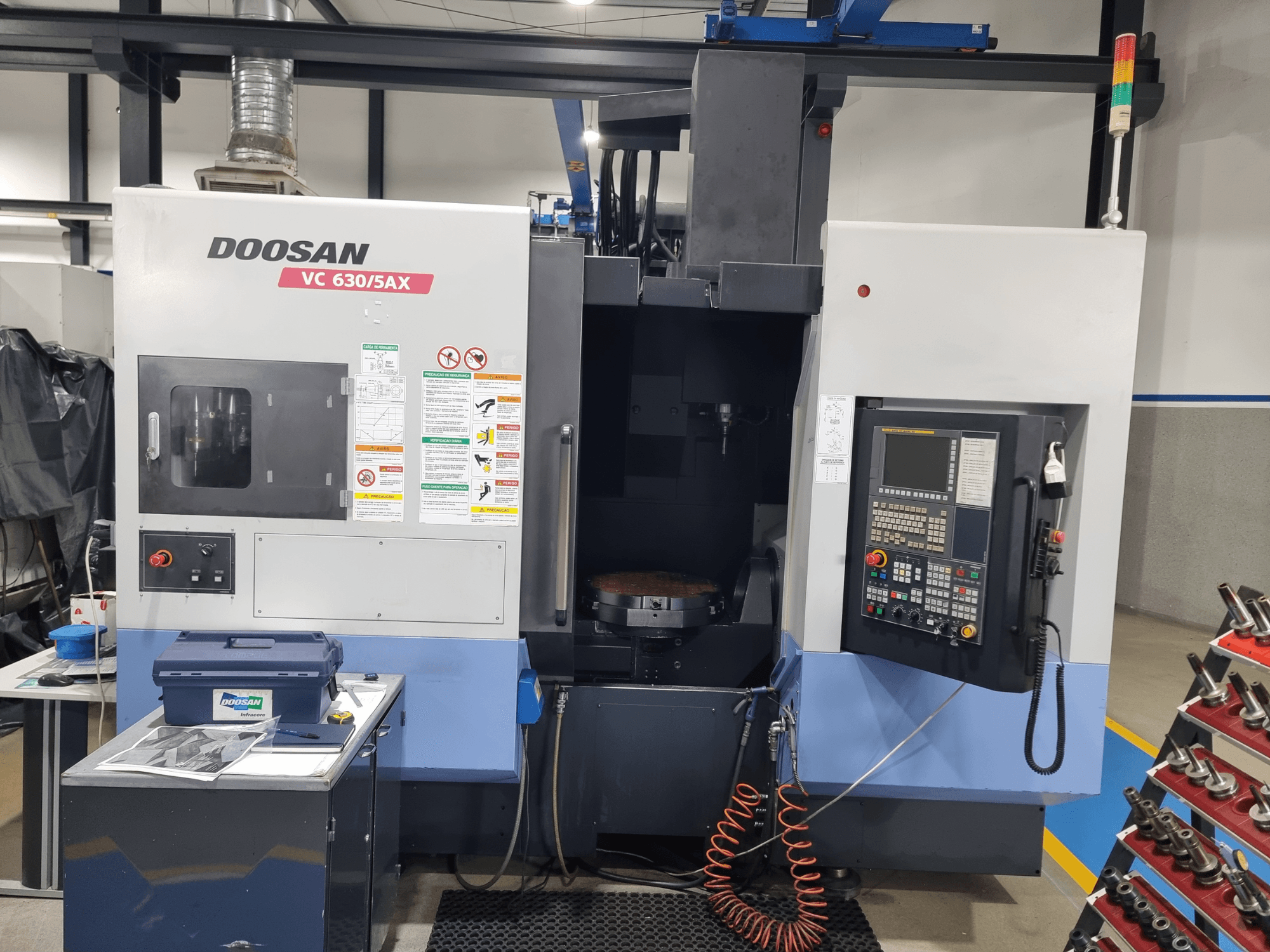 Универсальный обрабатывающий центр DOOSAN VC 630/5AX, вид спереди, на котором видны панель управления, зона резания и средства безопасности.