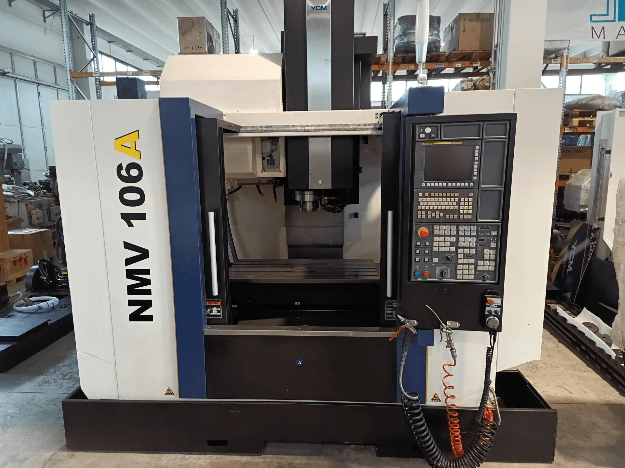 Обрабатывающий центр YCM NMV 106A, вид спереди, панель управления с кнопками и шланги подачи охлаждающей жидкости.