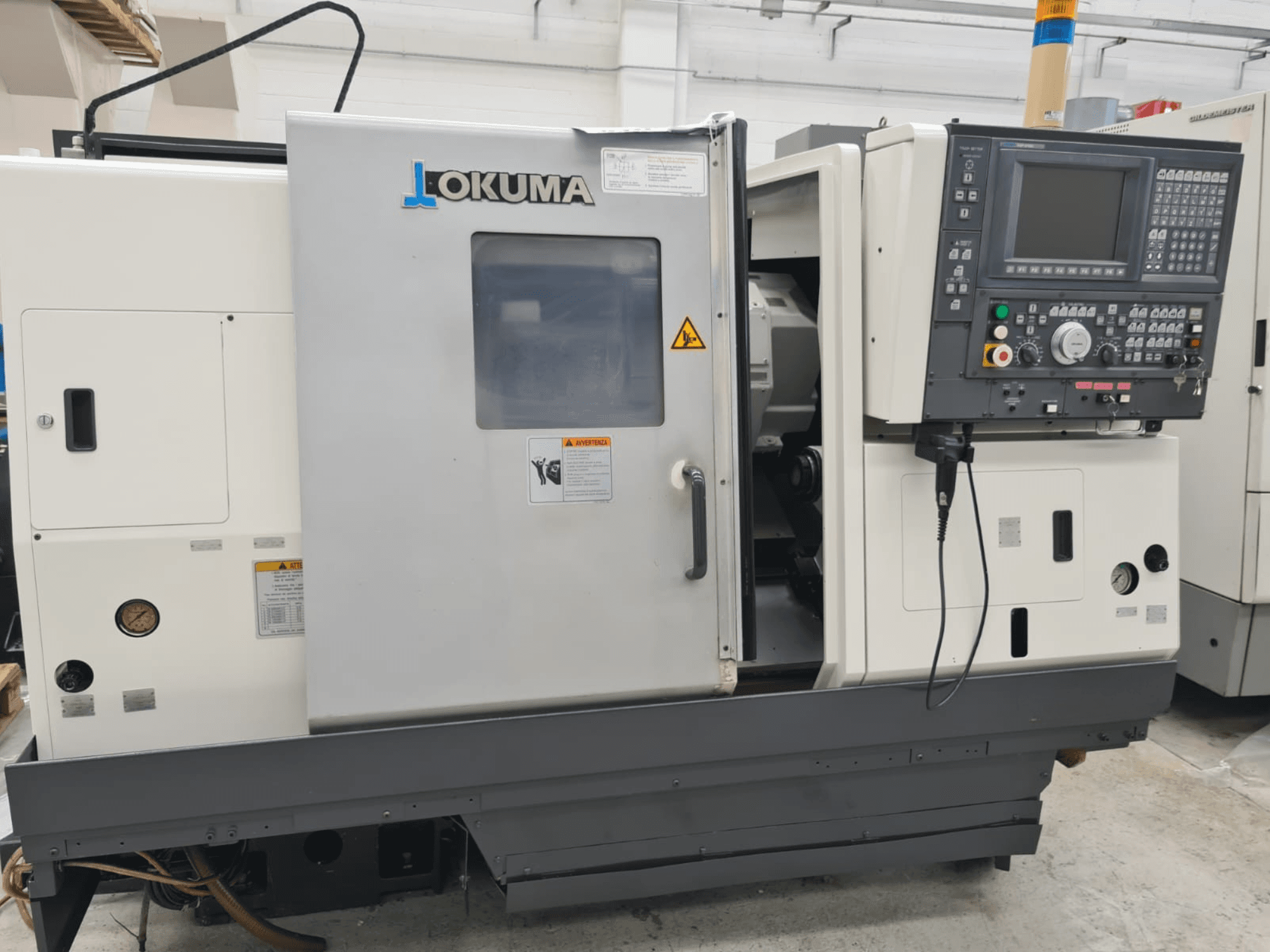 Горизонтальный токарный станок Okuma LB 300M X 500 вид сбоку, панель управления, доступ к шпинделю и предупреждения о безопасности.