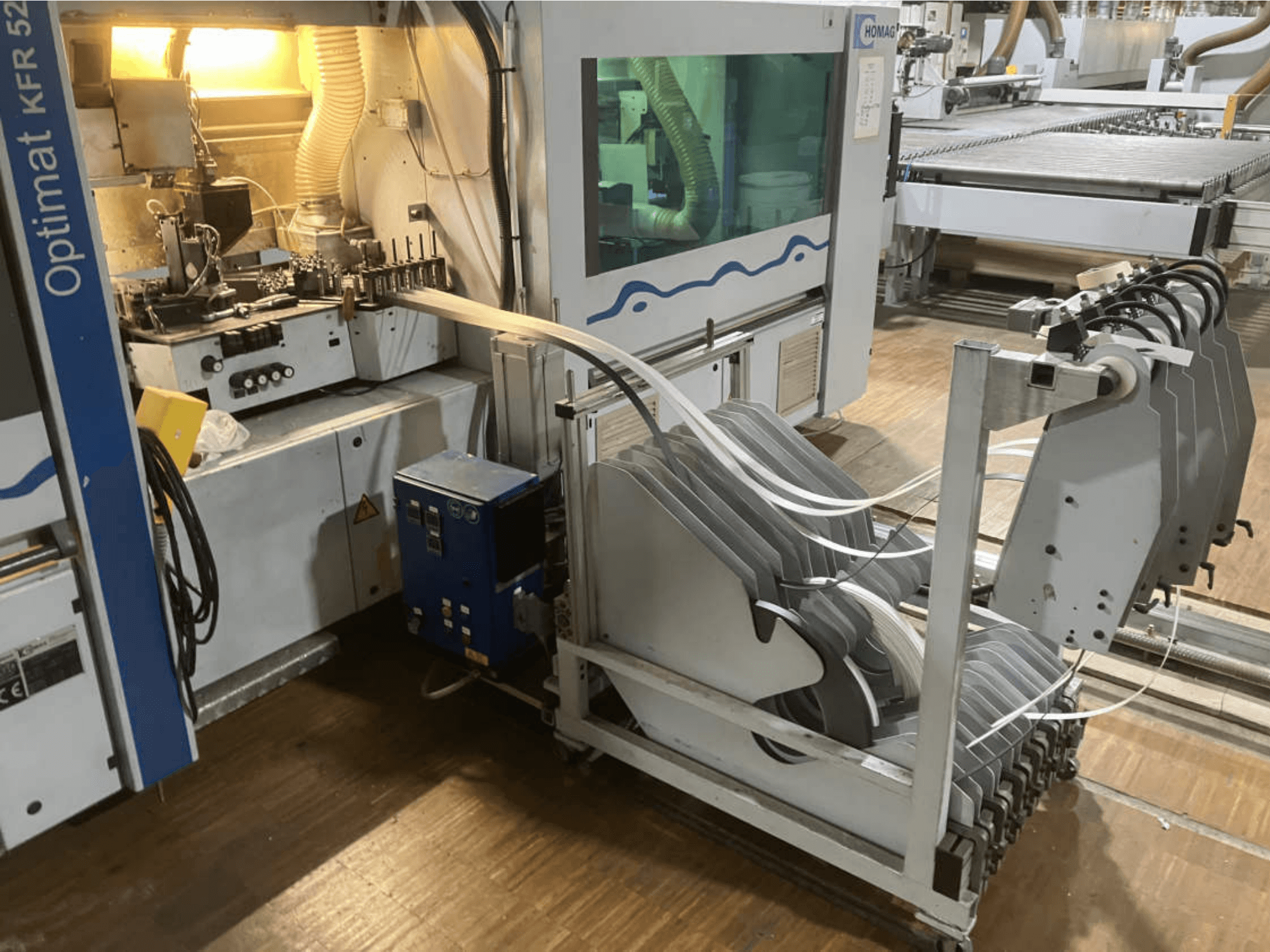 Двусторонний кромкооблицовочный станок HOMAG Optimat KFR 526/10/A3/35, вид сбоку, на котором видны панель управления и ролики для наклеивания кромок.