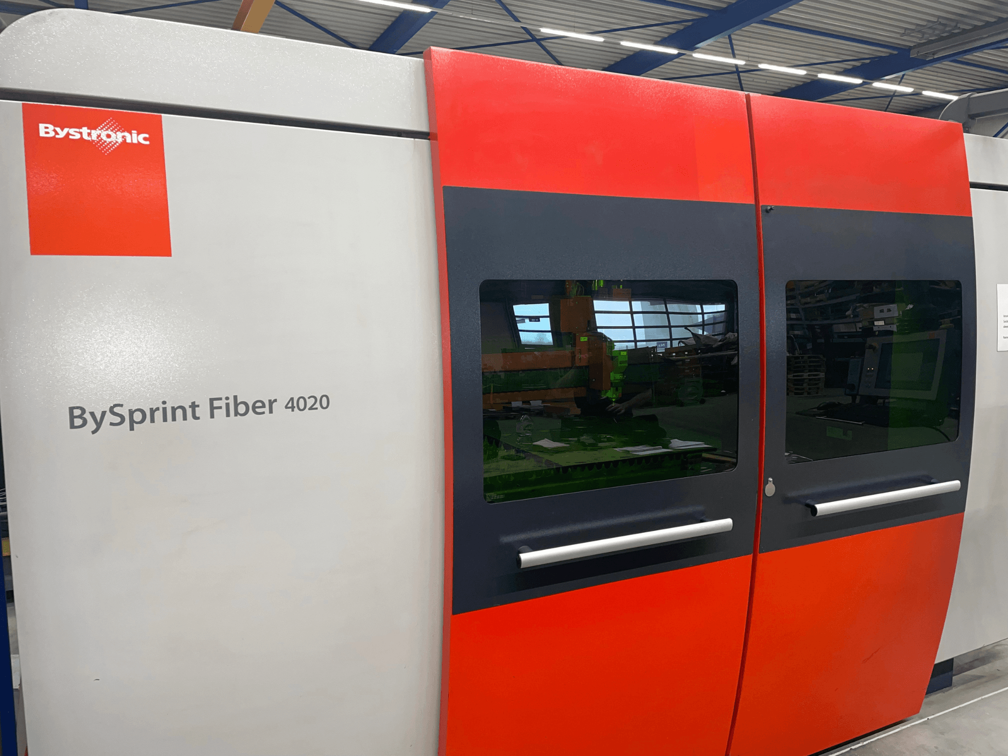 Bystronic BySprint Fiber 4020 на передней панели, выполненной в серо-красном цвете, с большими окнами и интерфейсом управления, видимым изнутри.