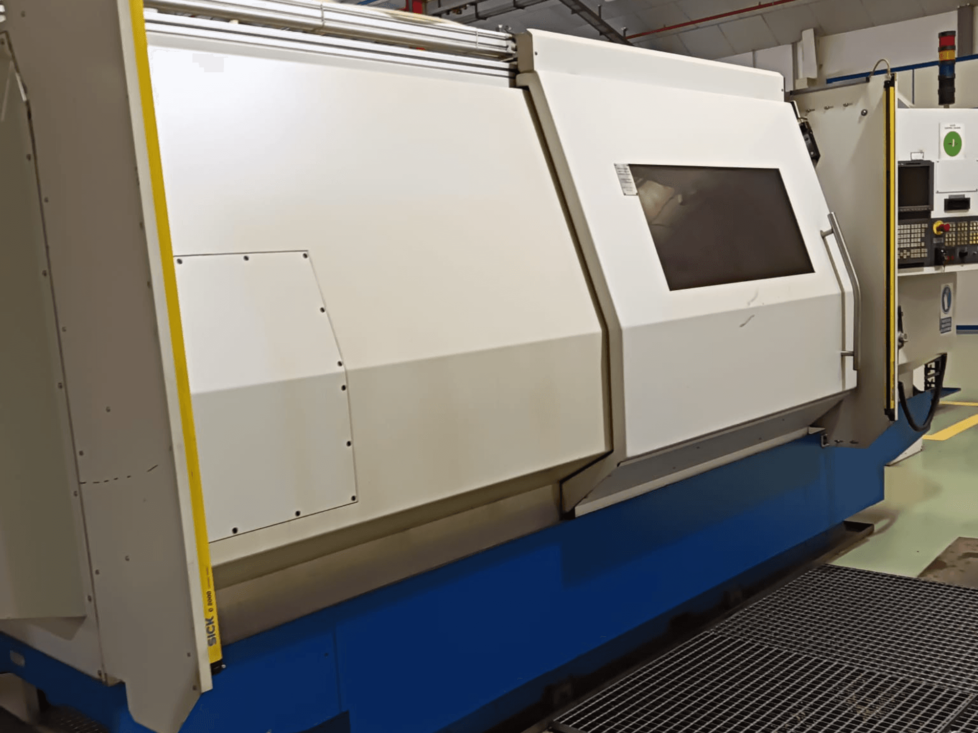 Промышленный токарный станок, вид сбоку, с большим бело-голубым корпусом, цифровой панелью управления и защитными элементами.