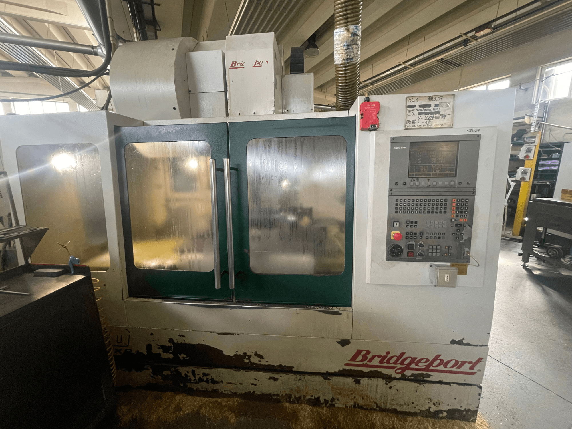 Вертикальный обрабатывающий центр Bridgeport VMC 1000/30, вид спереди с панелью управления; видно изношенную внешнюю поверхность и зеленые дверцы.