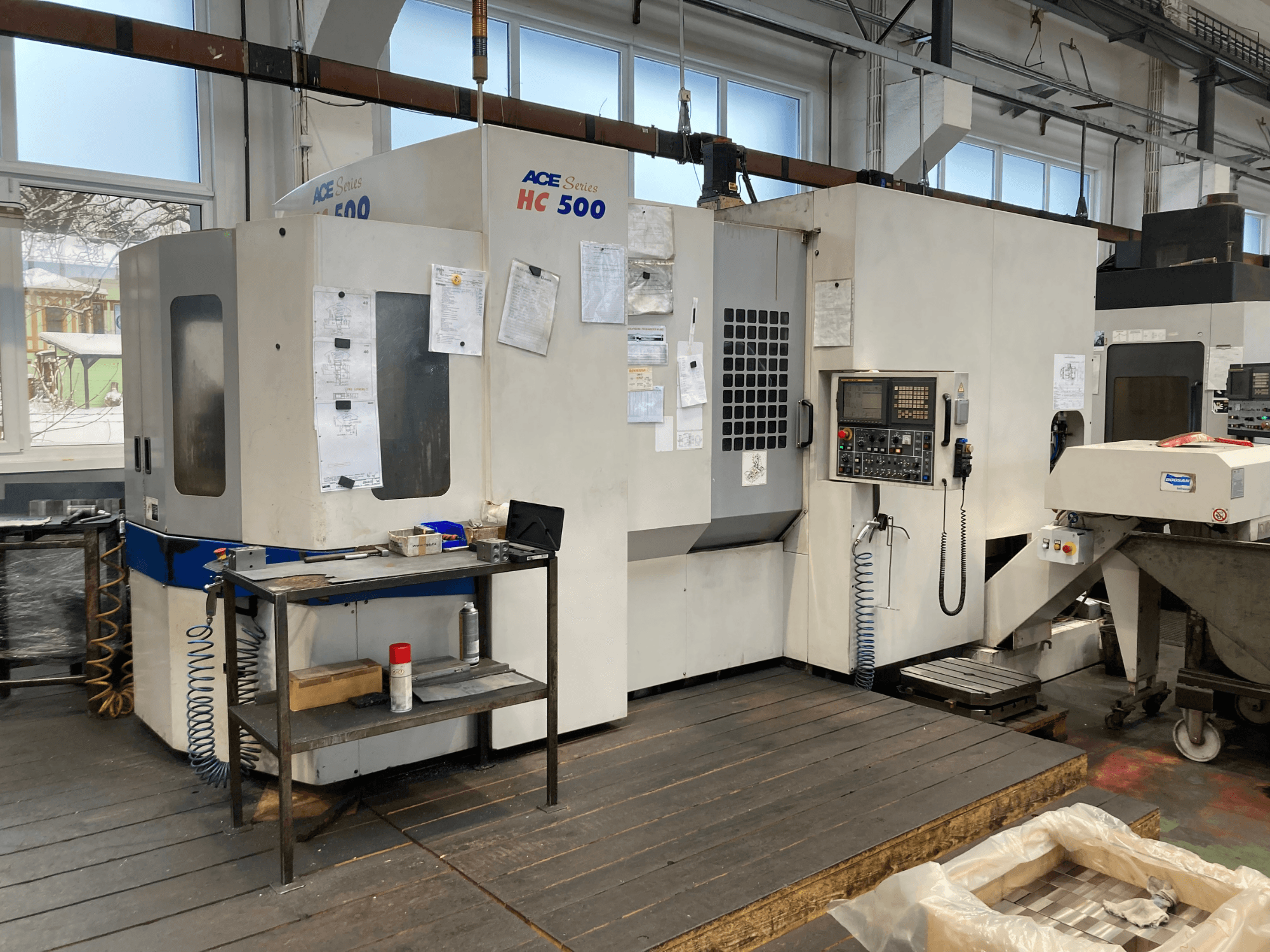 Горизонтальный обрабатывающий центр DOOSAN ACE HC-500, вид спереди; панель управления, множество хранилищ для инструментов и промышленные настройки.