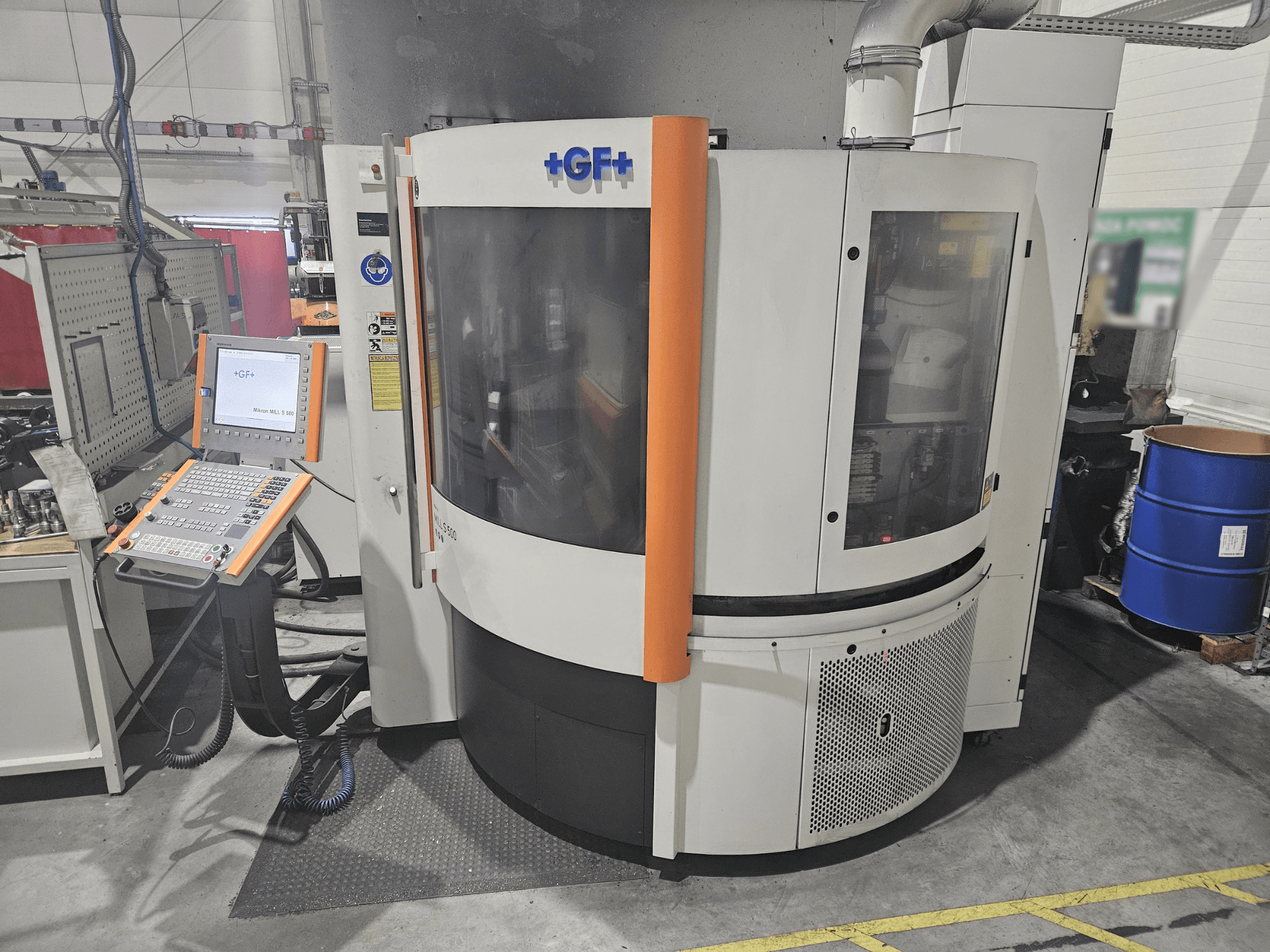 Станок GF Machining Solutions с панелью управления, вид спереди; прозрачная панель, оранжевые акценты и промышленная обстановка.