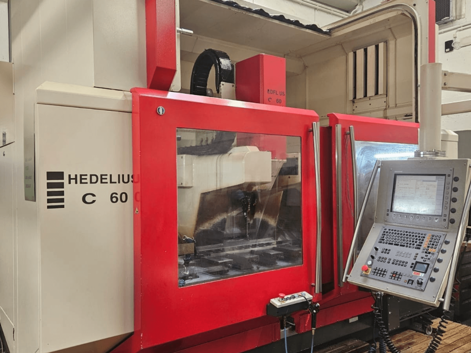 Вертикальный обрабатывающий центр HEDELIUS C60 сбоку, с красной передней панелью и консолью управления с дисплеем.