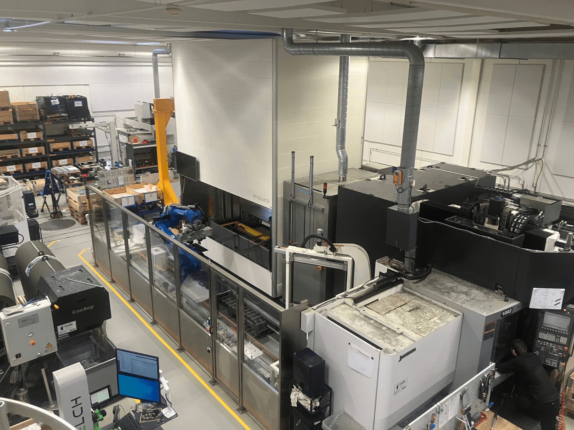 Система автоматизации SSI SCHAFER Logimat на складе, вид спереди; роботизированная рука, стеллажи и оборудование.