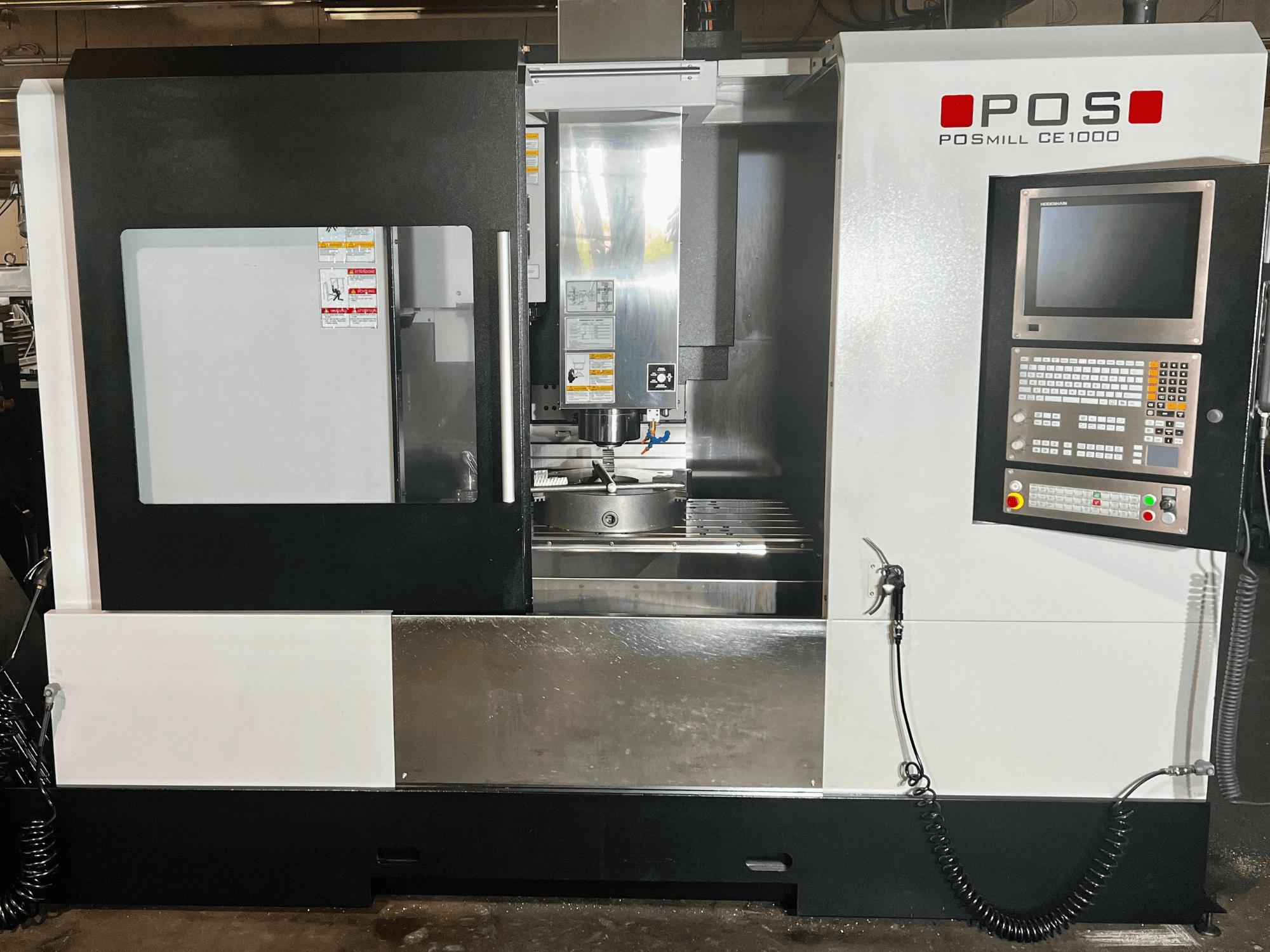 Вид спереди вертикального обрабатывающего центра POSmill CE1000 с панелью управления, окном и металлическими поверхностями.