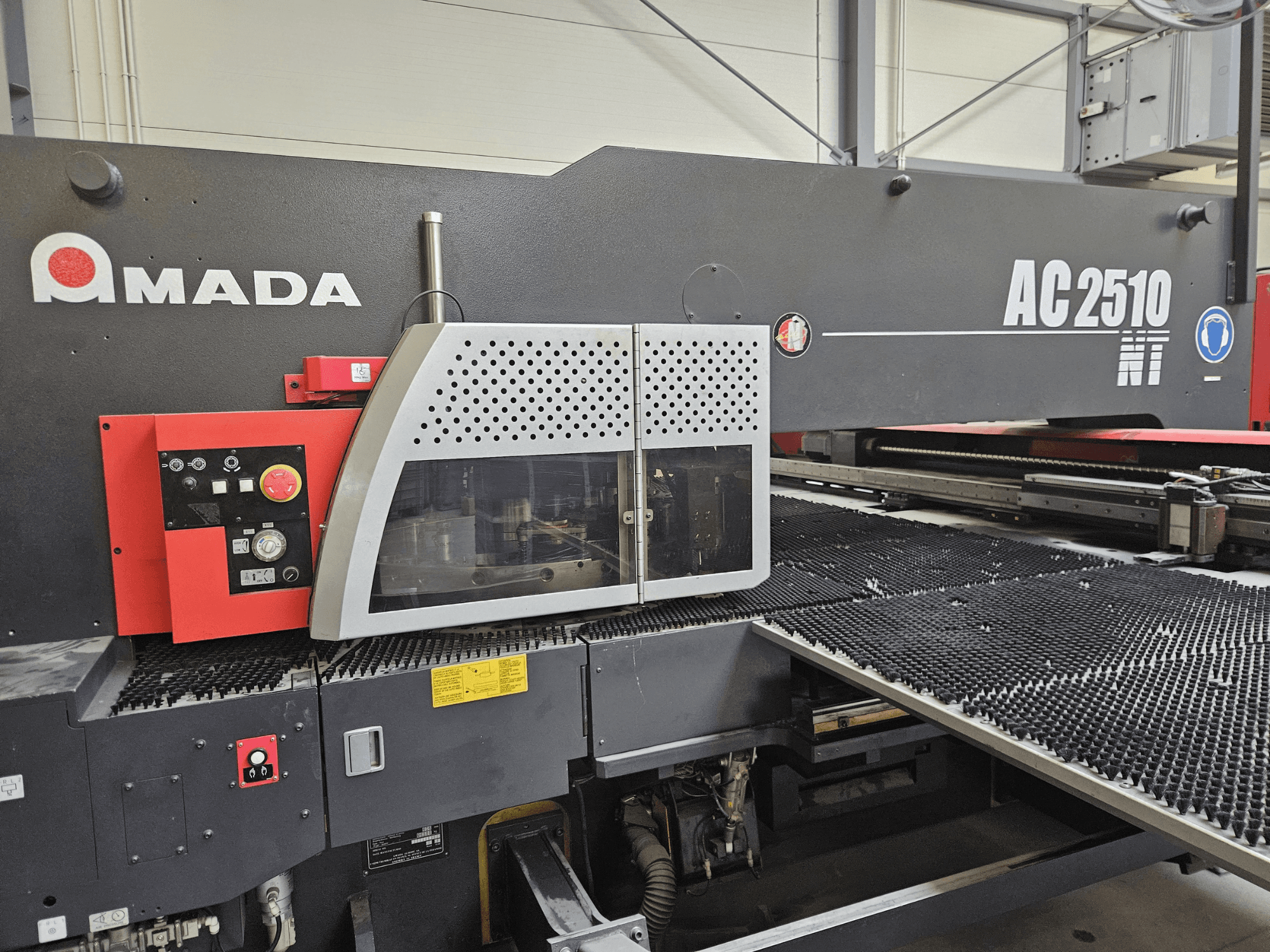 Станок лазерной резки Amada AC2510 NT, вид спереди, панель управления с ручками, кнопками и защитной крышкой.
