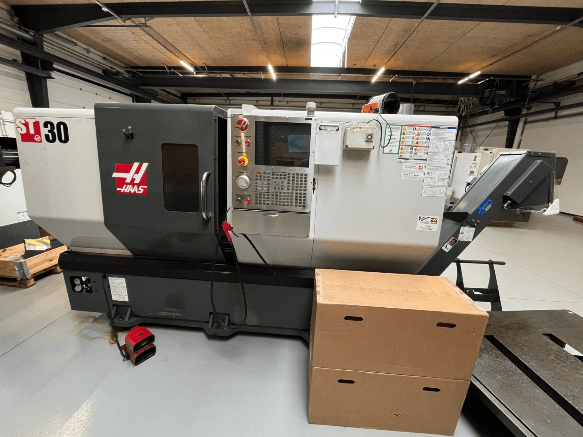 Токарный станок с ЧПУ Haas ST-30, вид спереди, панель управления с кнопками, аварийная остановка и две сложенные картонные коробки.