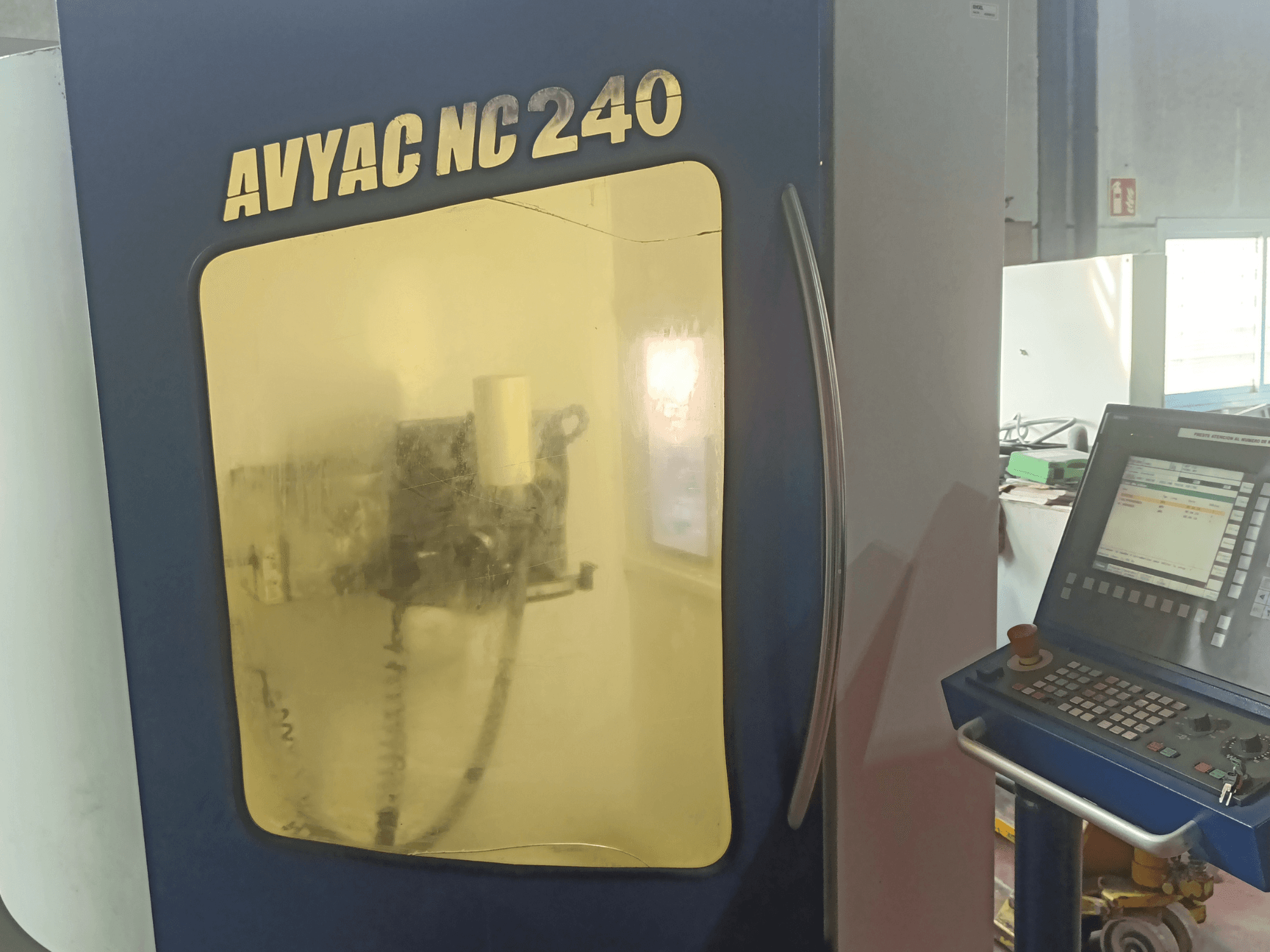 Круглошлифовальный станок AVYAC NC240, вид сбоку с изображением панели управления и частично видимой через окно зоны шлифования.