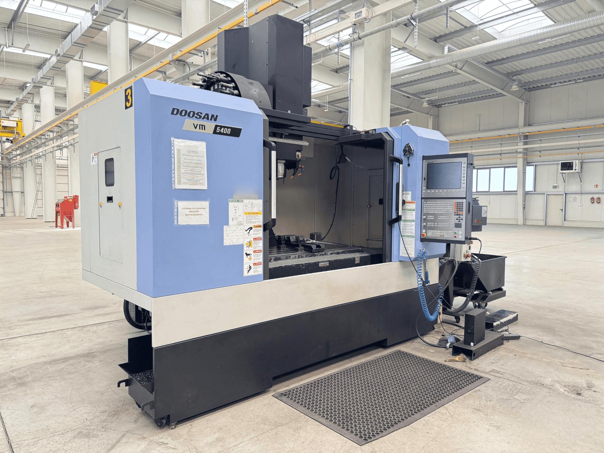 Вертикальный обрабатывающий центр DOOSAN VM 5400, вид спереди, демонстрирующий панель управления и рабочую зону в просторном промышленном помещении.