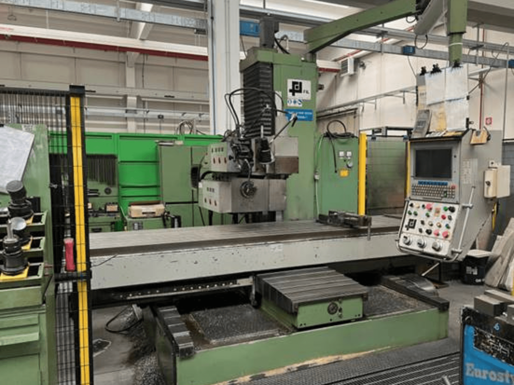 Промышленный фрезерный станок JFL, вид спереди с панелью управления, большим плоским столом и металлической стружкой на полу.