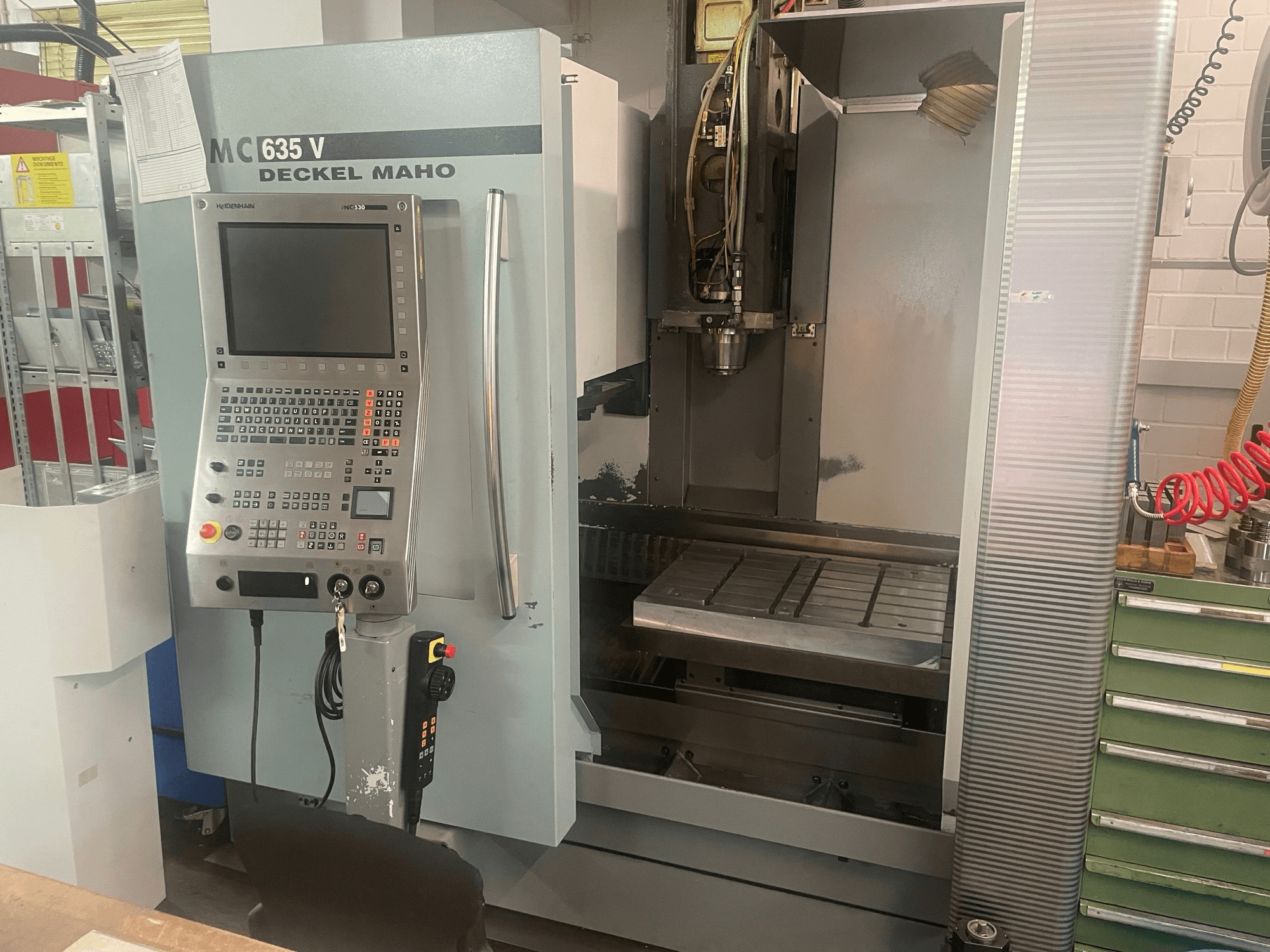 Вид спереди на вертикальный обрабатывающий центр DECKEL MAHO DMC 635 V с панелью управления и открытой рабочей зоной, на котором видны инструментальная головка и станина.