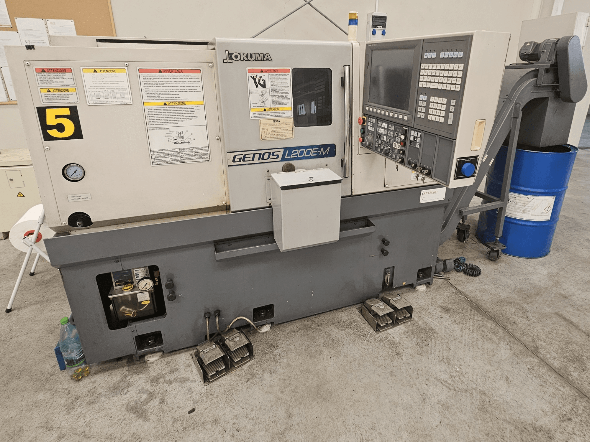 Горизонтальный токарный станок Okuma GENOS L200E-M с видом спереди, панель управления, наклейки и бочка с охлаждающей жидкостью.