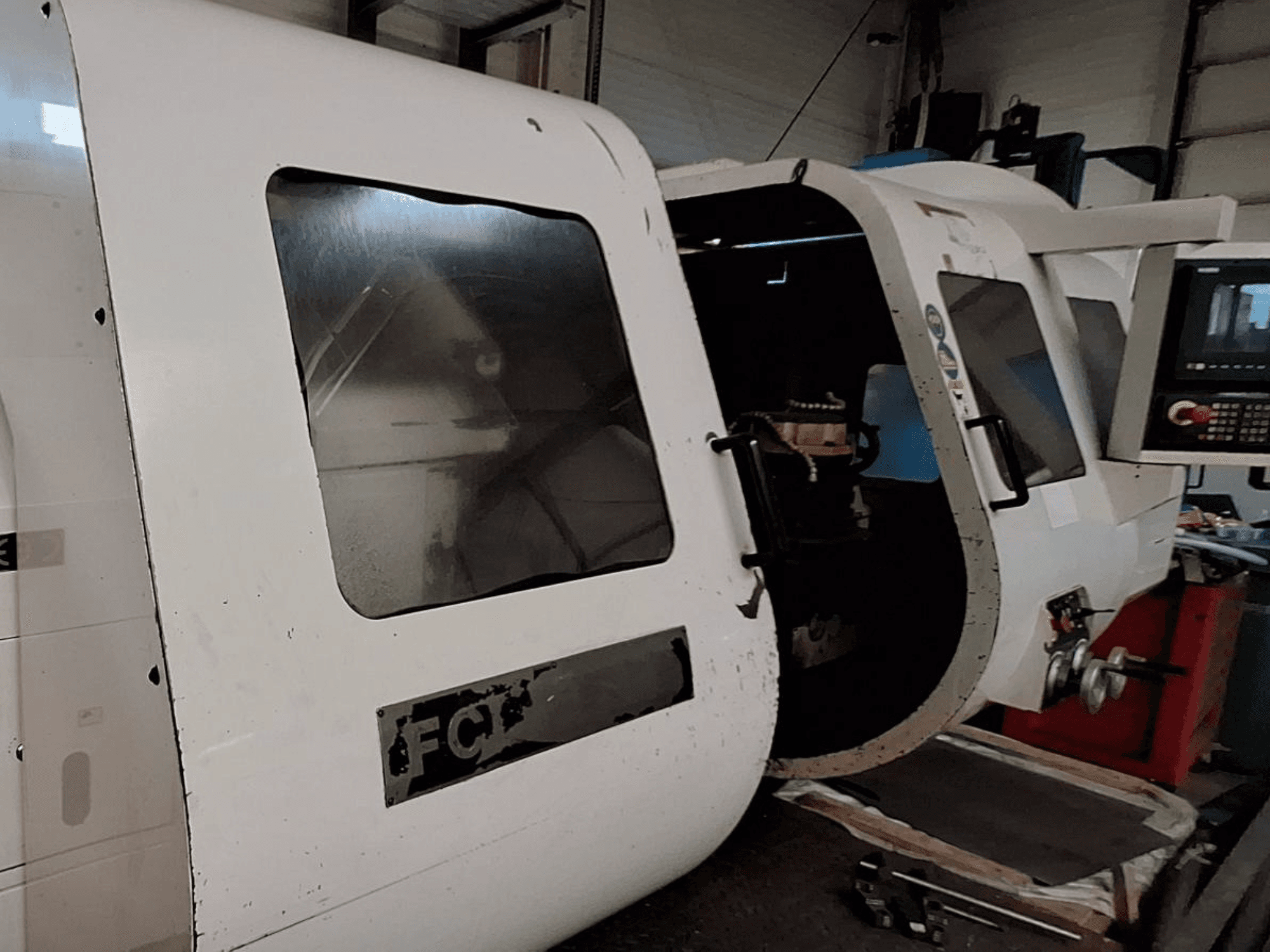 Белый станок с ЧПУ с видимой панелью управления и открытой дверцей, демонстрирующей внутренние компоненты; вид спереди. Бренд: FCT.