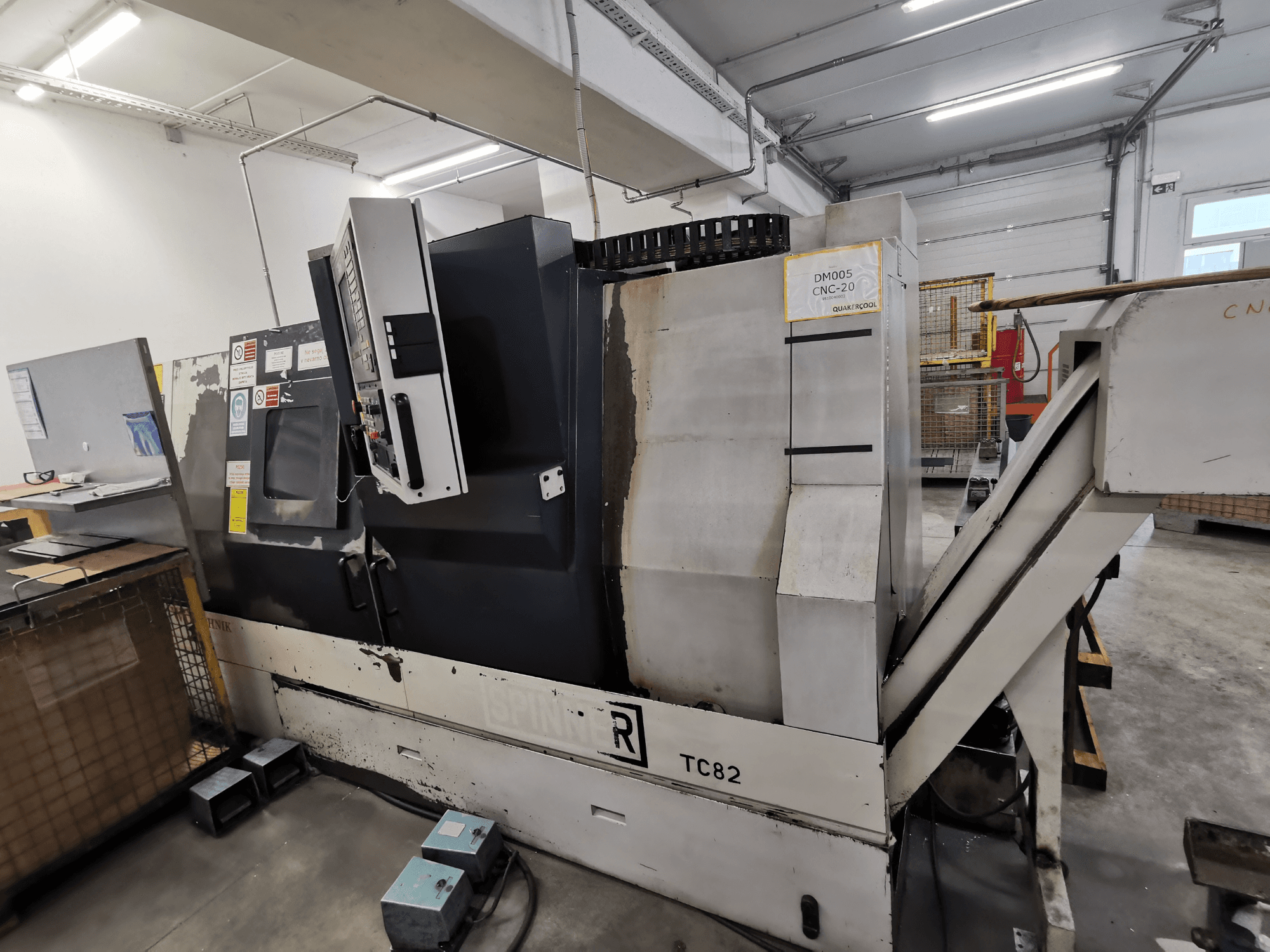 Станок с ЧПУ, марка Spinner, модель TC82, вид сбоку, показывающий панель управления и желоб для удаления лома в мастерской.