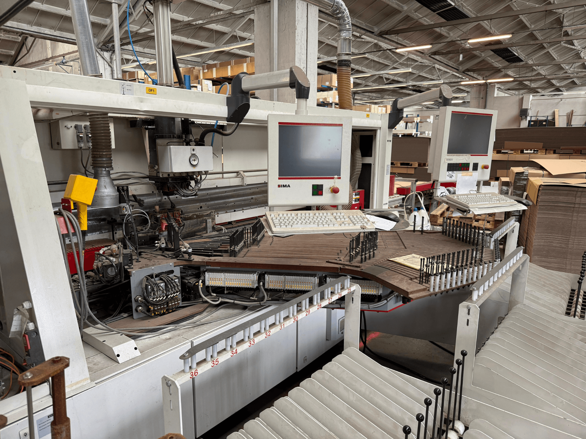Прецизионный деревообрабатывающий станок IMA с двумя мониторами и панелями управления, вид спереди с изображением конвейера и зоны инструмента.