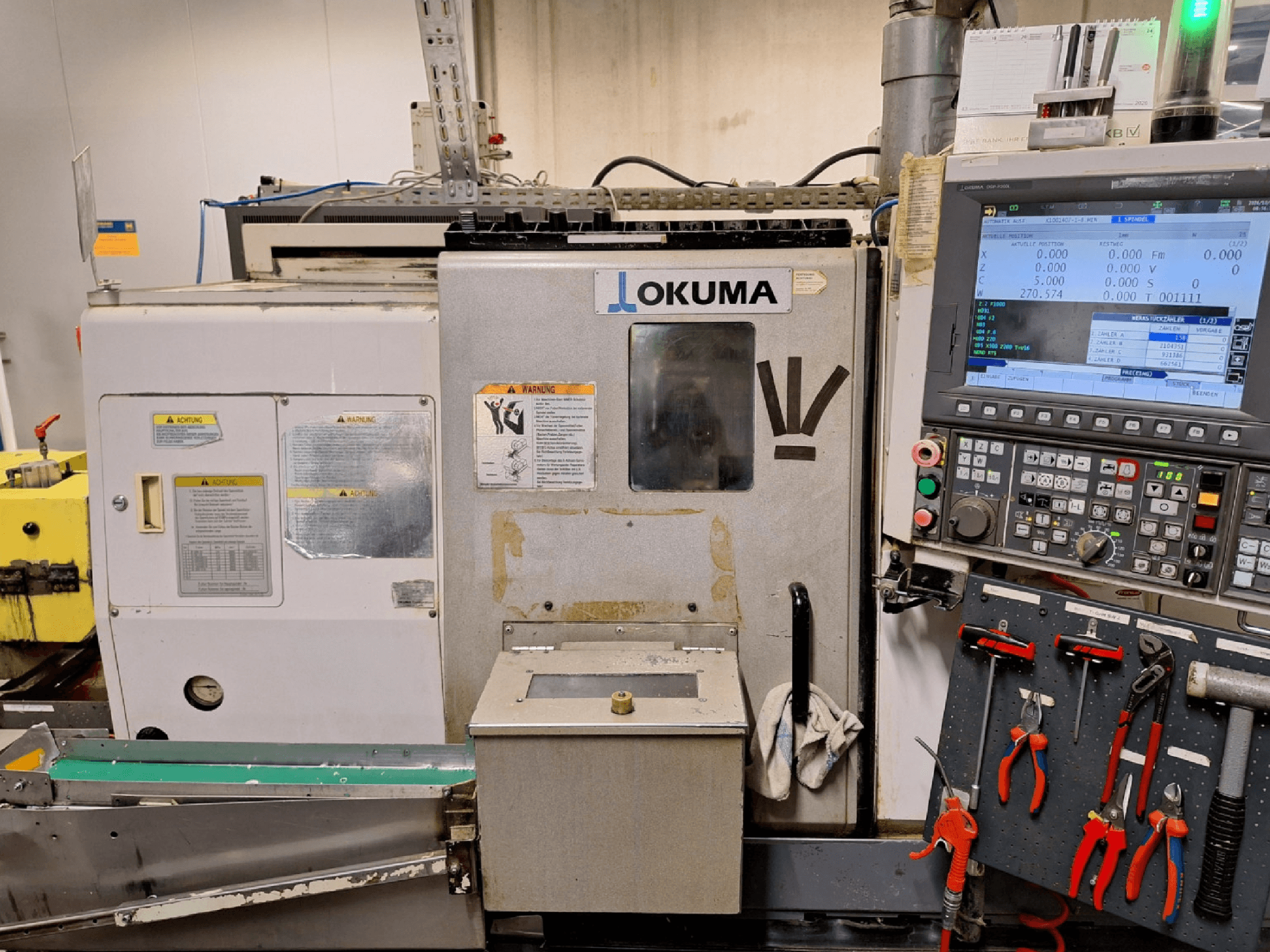 Горизонтальный токарный станок Okuma LB200-MW, вид спереди, с панелью управления и инструментами, видимыми сбоку.