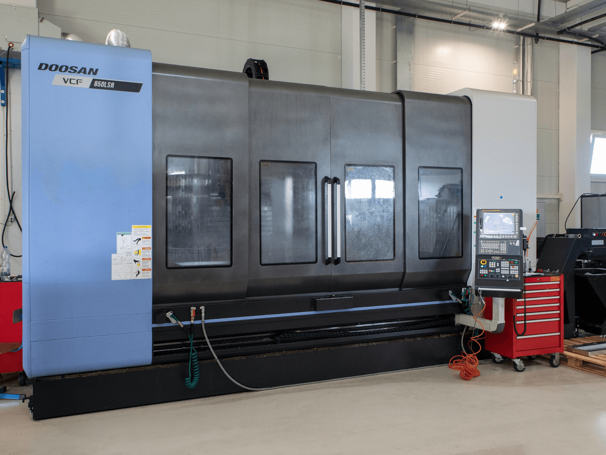 Токарно-фрезерный центр DOOSAN VCF850, вид спереди; оснащён большими двойными окнами, панелью управления и отсеком для хранения инструментов. Идеально подходит для механической обработки.