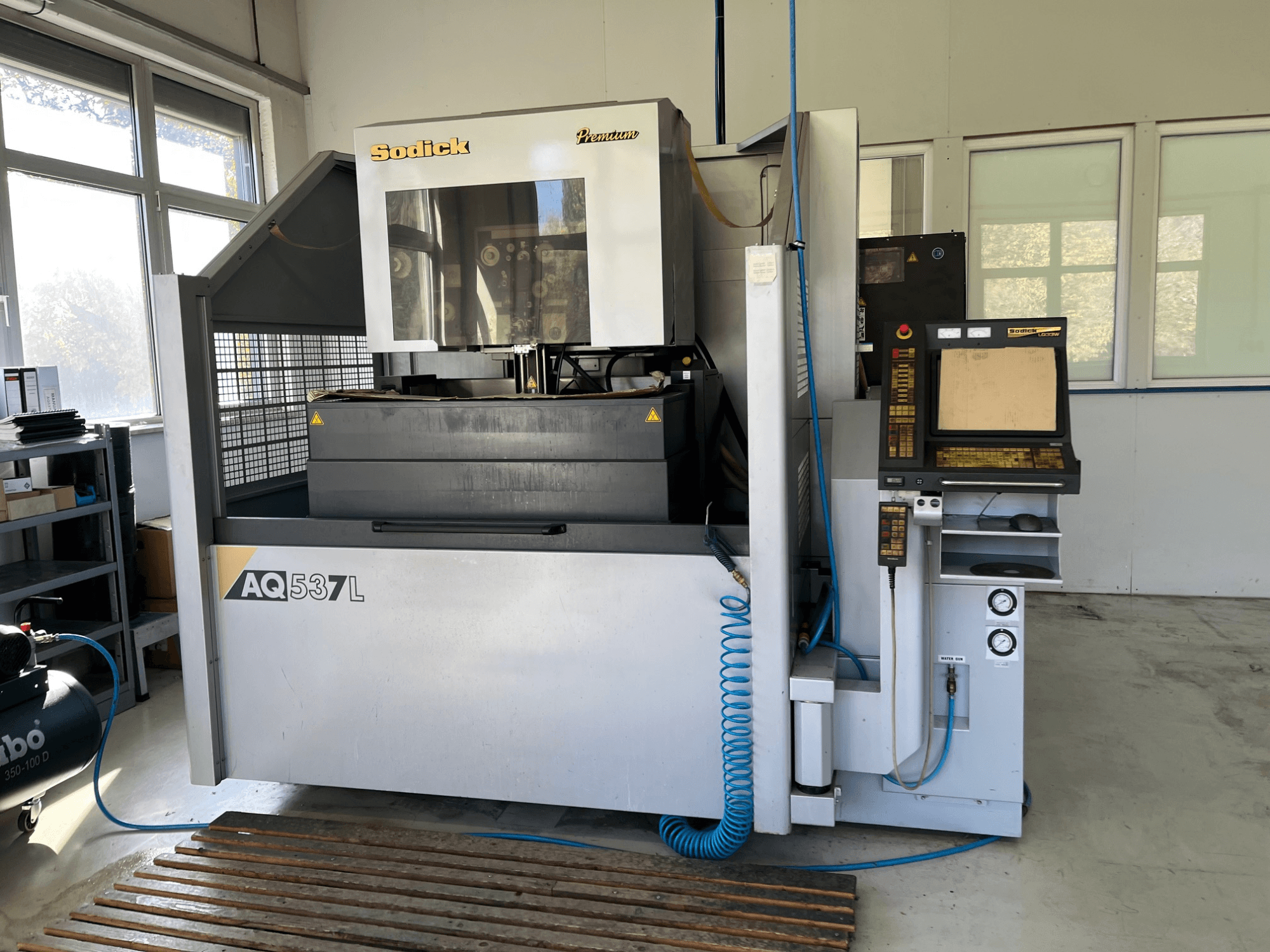 Электроэрозионный станок (ЭЭМ) Sodick AQ537L на переднем плане, панель управления, линии водяного охлаждения и рабочее пространство.