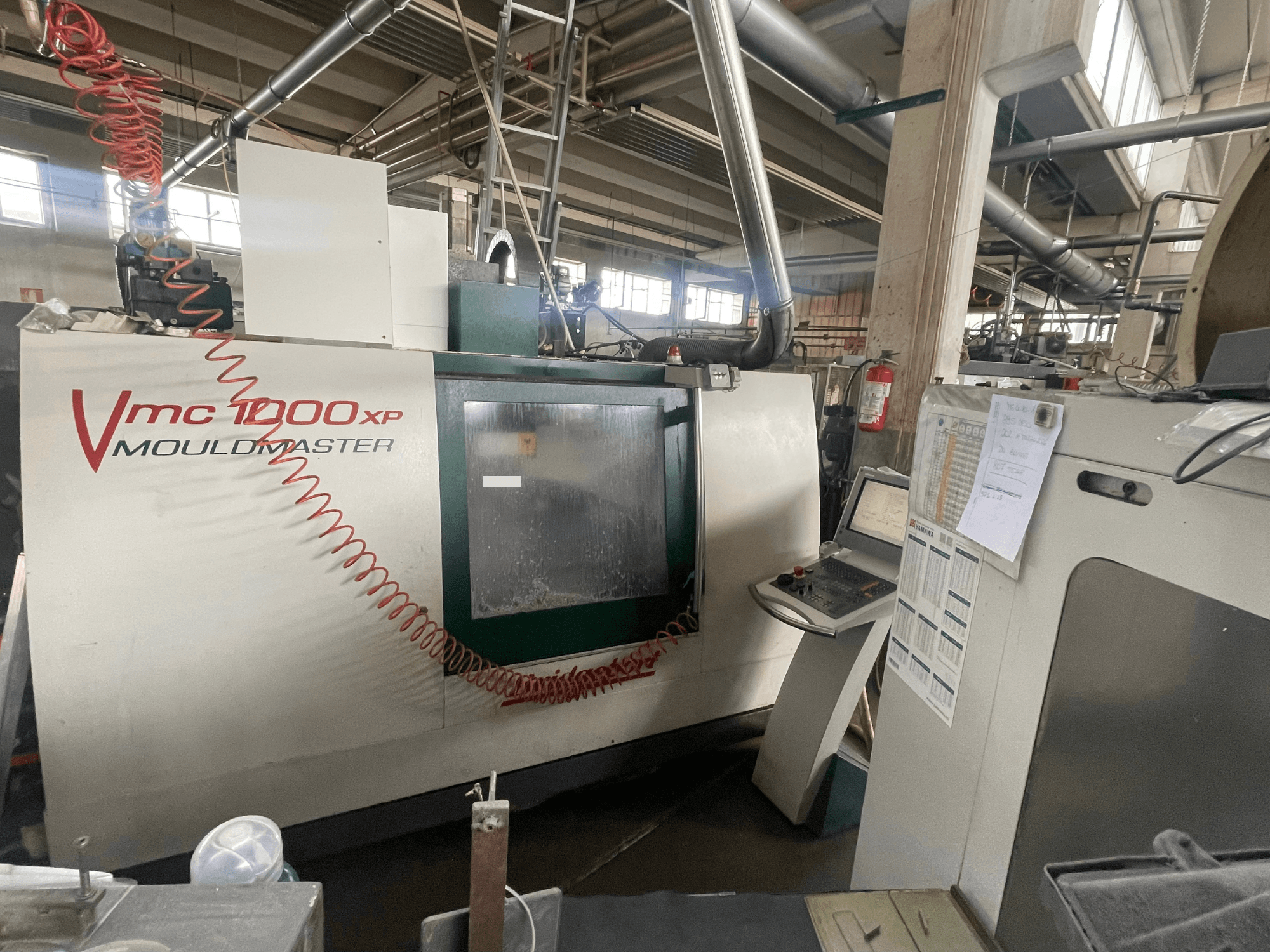 Вертикальный обрабатывающий центр Bridgeport VMC 1000, вид спереди, на котором видны панель управления и детали станка в промышленной обстановке.