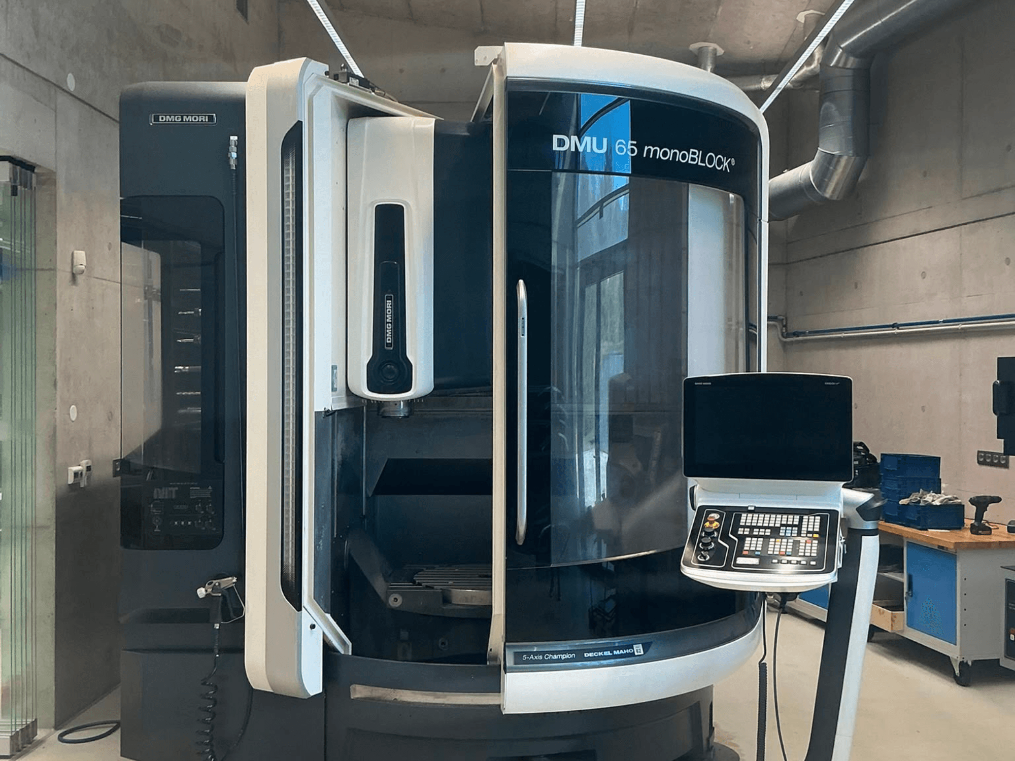 Вертикальный обрабатывающий центр DMG MORI DMU 65 monoBLOCK, вид спереди, с изображением панели управления и деталей станка в условиях цеха.