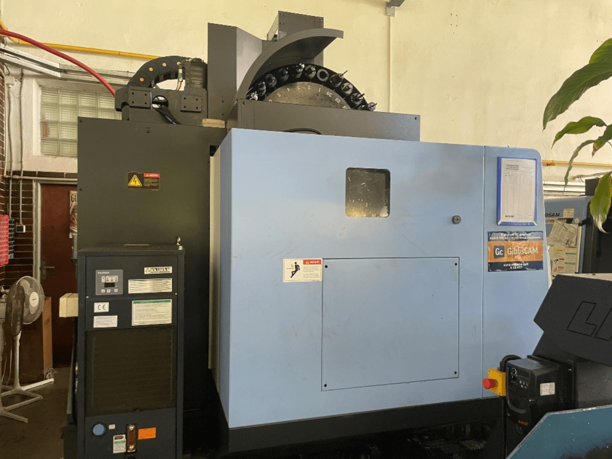 Вид спереди вертикального обрабатывающего центра DOOSAN DNM 5700 с панелью управления, наклейками безопасности и характеристиками станка.