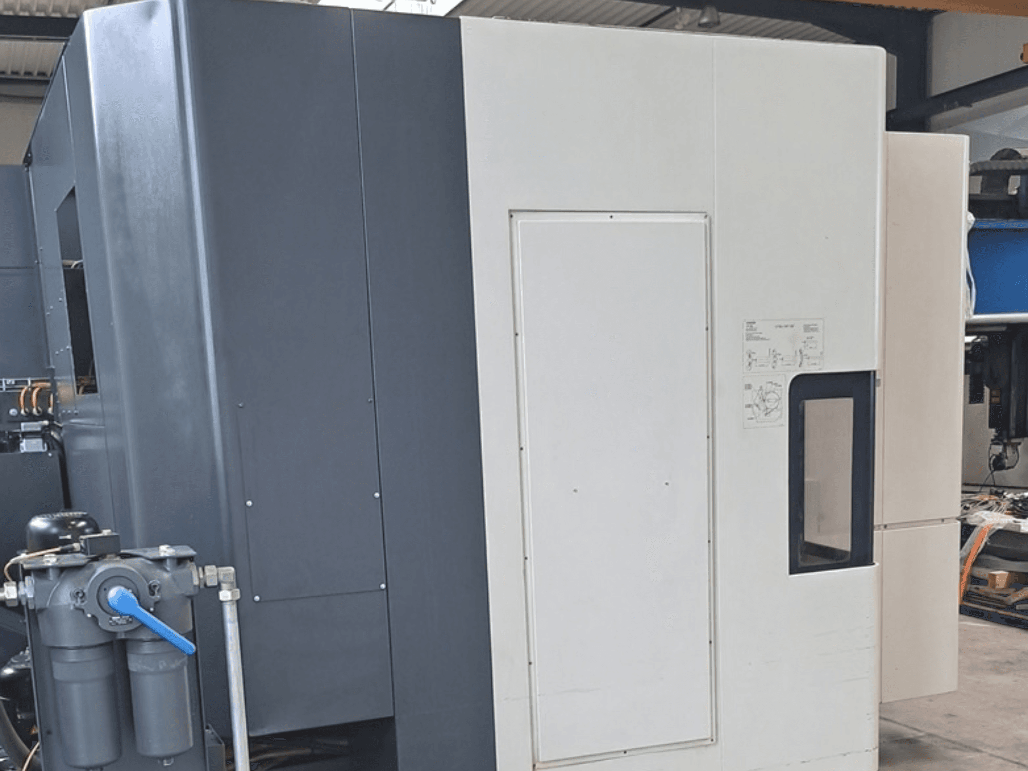 Горизонтальный обрабатывающий центр DMG MORI NHX5000, вид сбоку с панелью управления и механическими элементами.