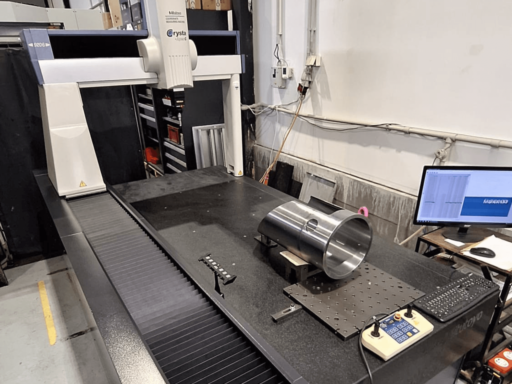 КИМ Mitutoyo Crysta-Apex C9206 на виде спереди, измерение цилиндрической металлической детали на плите из черного гранита.