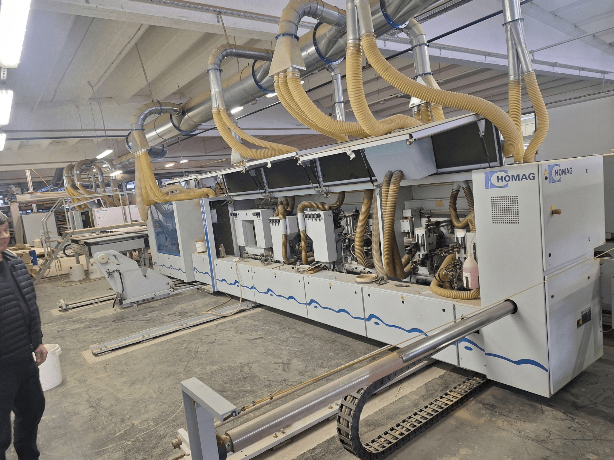 Деревообрабатывающий станок HOMAG в заводских условиях, вид спереди с несколькими шпинделями и системой пылеудаления.