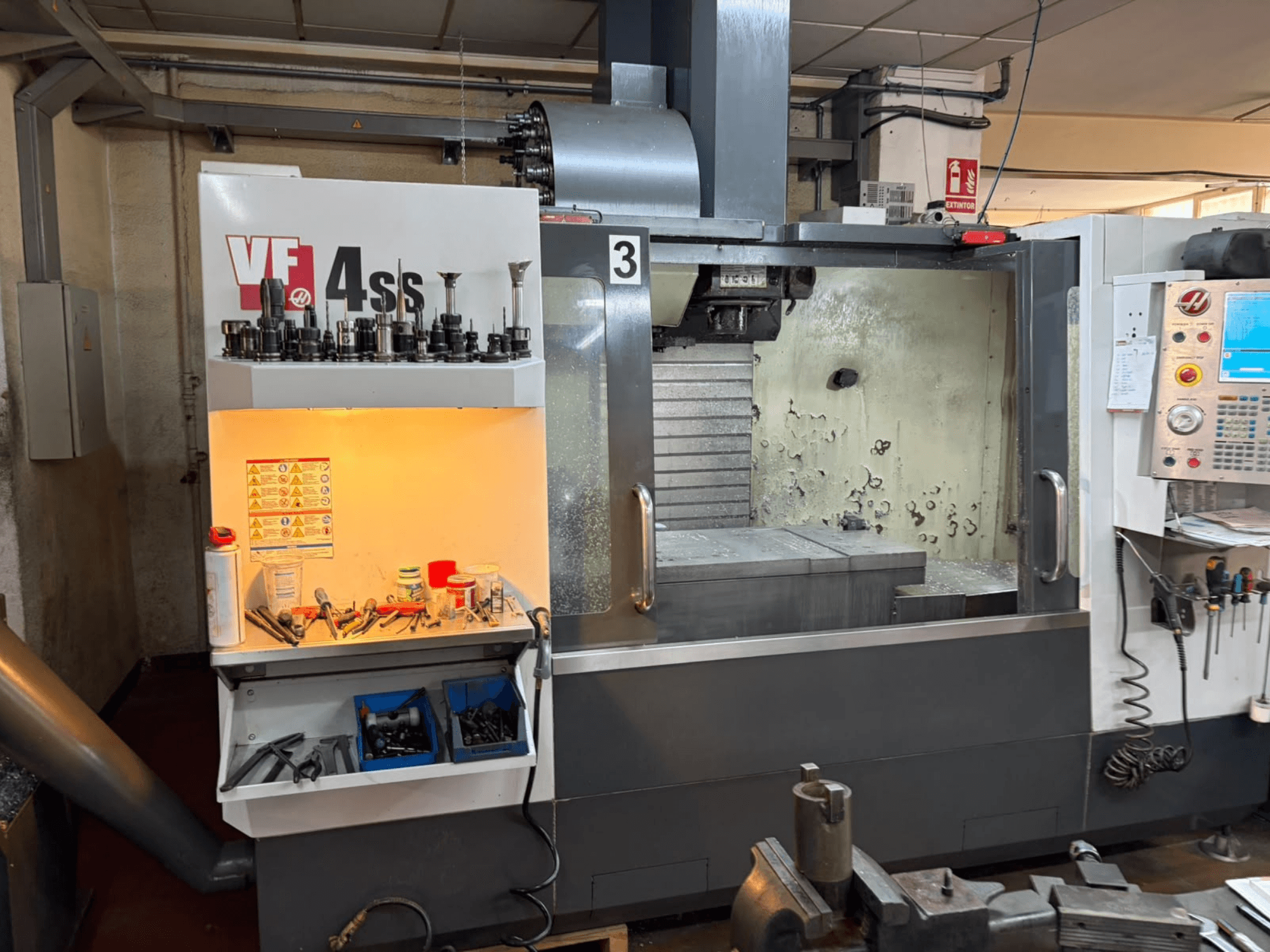 Вертикальный обрабатывающий центр HAAS VP 4SS, вид спереди, с изображением хранилища инструментов, панели управления и рабочей зоны с деталями обработки.