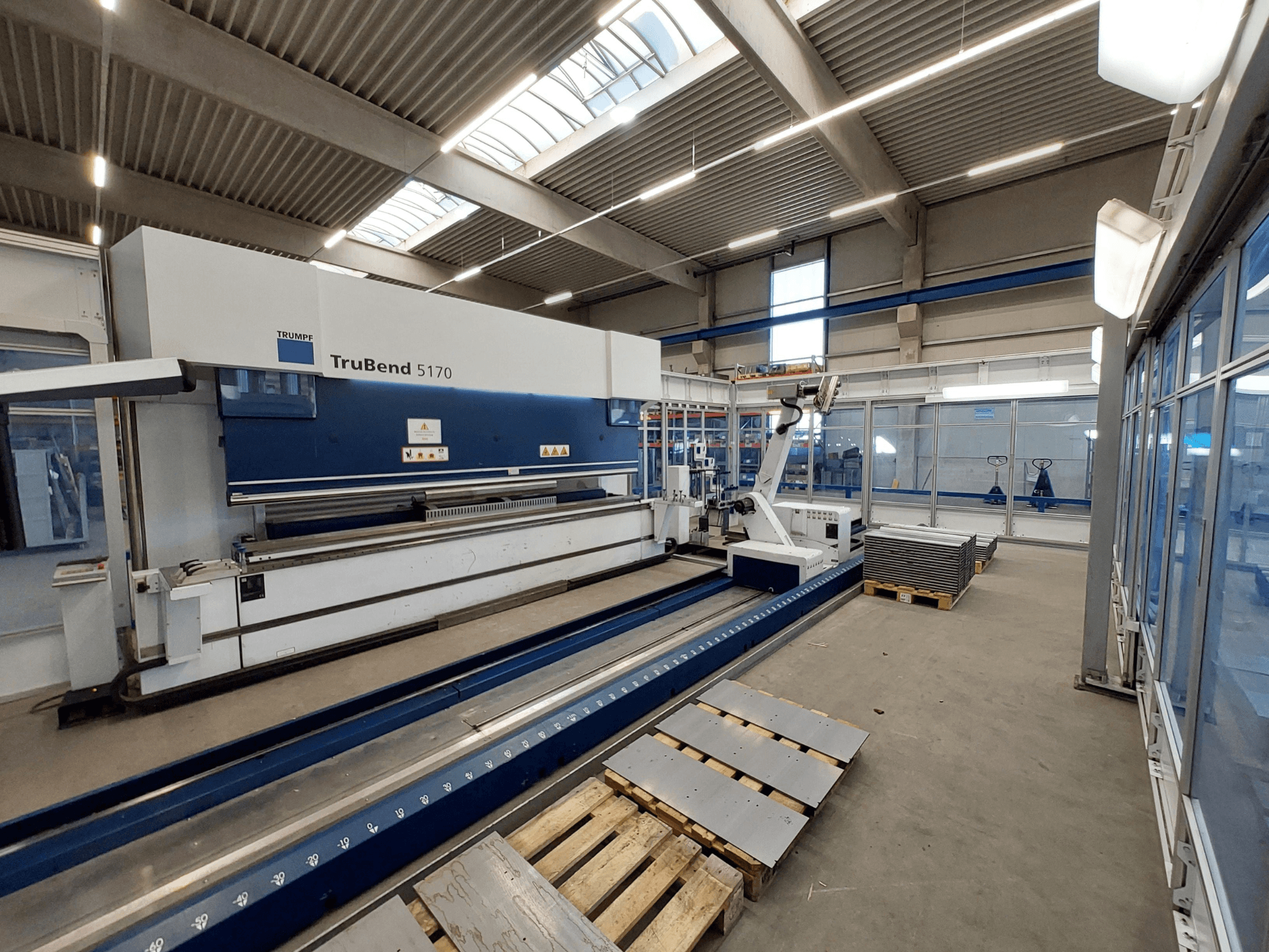 Листогибочный пресс TRUMPF TruBend 5170 в цеху, вид сбоку, демонстрирующий гибочный инструмент и уложенные на поддоны металлические листы.