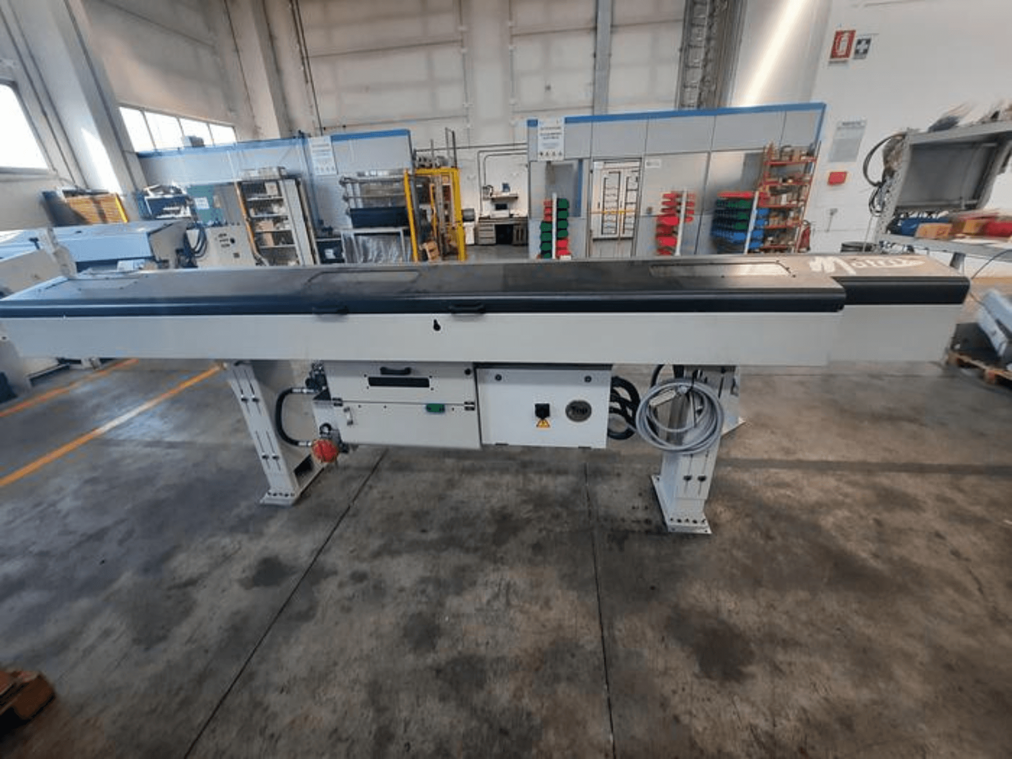 Металлический конвейерный стол с гладкой черной столешницей, вид сбоку, с кнопками управления и кабелями; логотип бренда виден частично.