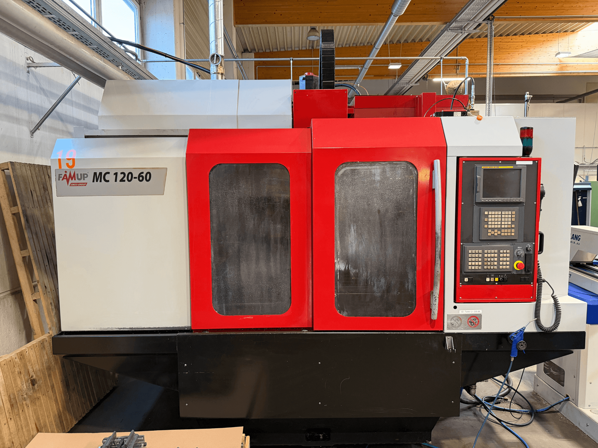 Вид спереди вертикального обрабатывающего центра EMCO MC 120-60 с красно-белым корпусом, панелью управления и экраном.