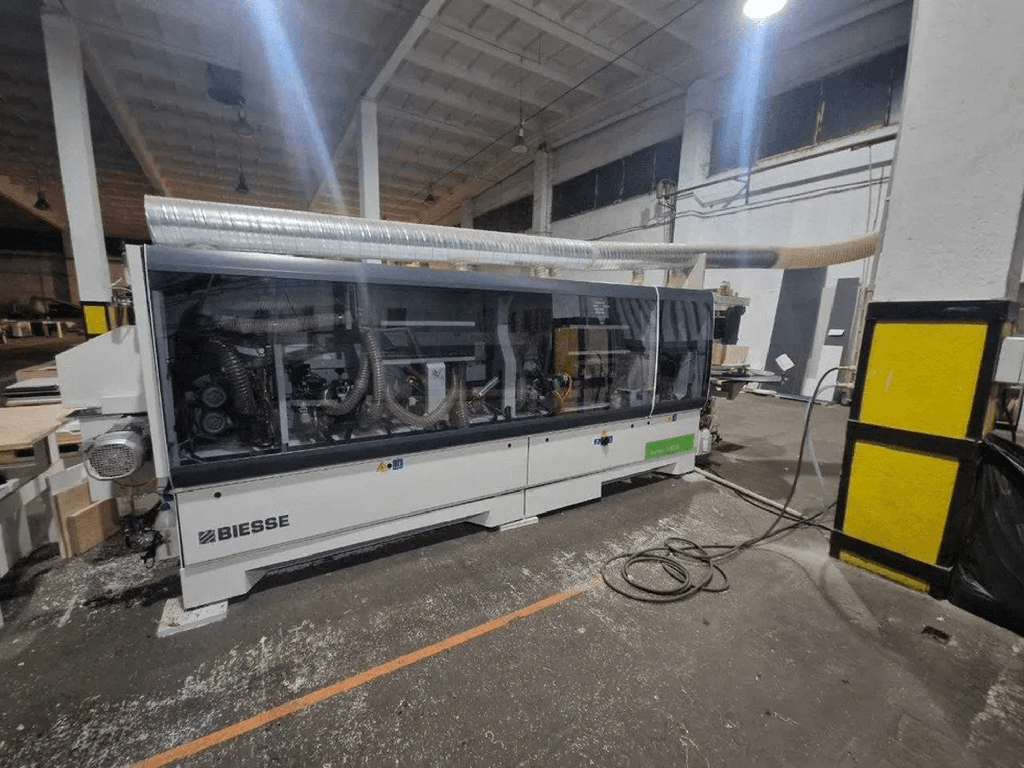 Кромкооблицовочная машина BIESSE Akron 1440 A в цехе, с прозрачной крышкой и открытыми для обзора механическими узлами.